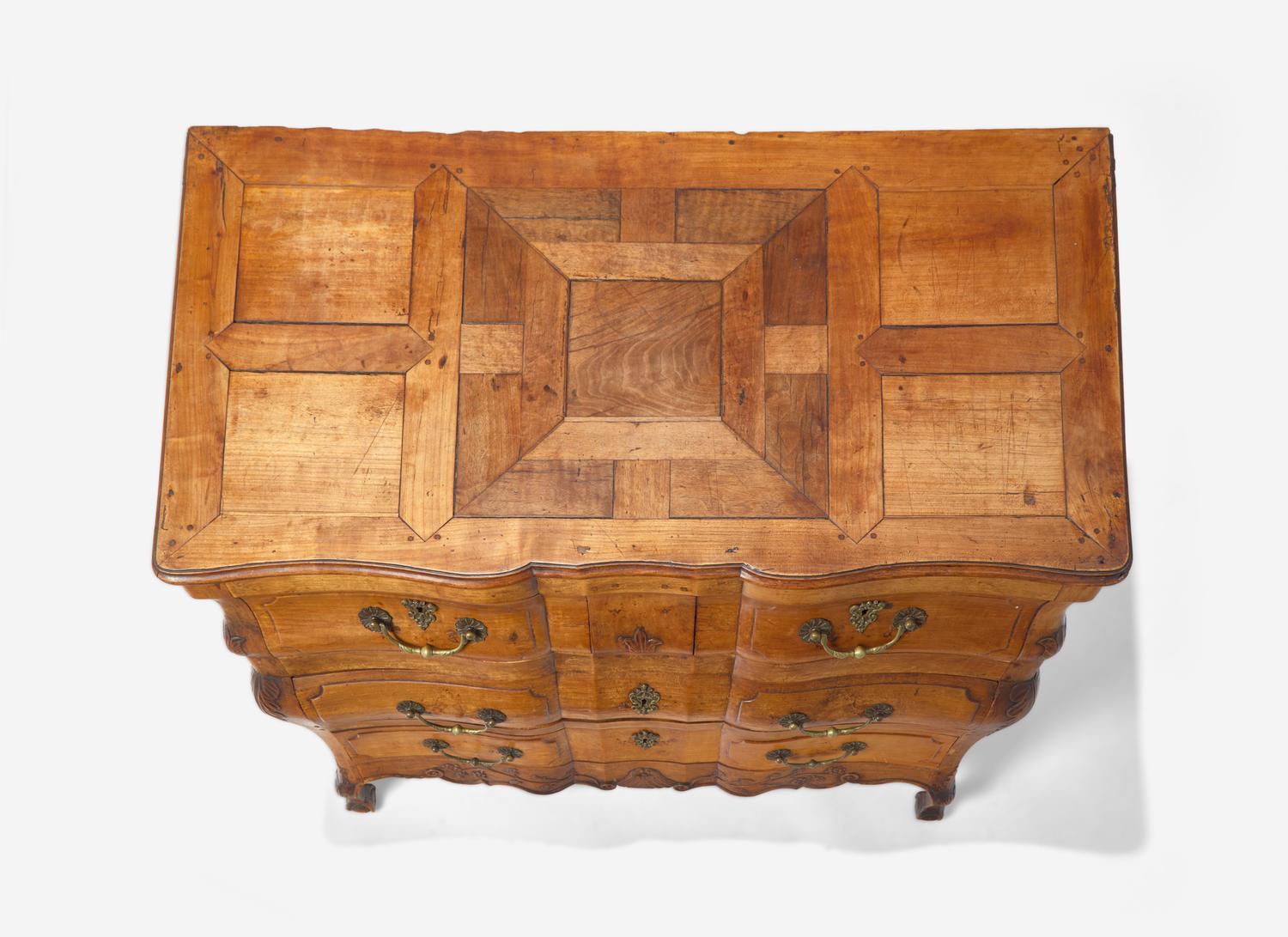 A Louis XV Provincial Carved Fruitwood Serpentine and Paneled-Top Bombé Commode