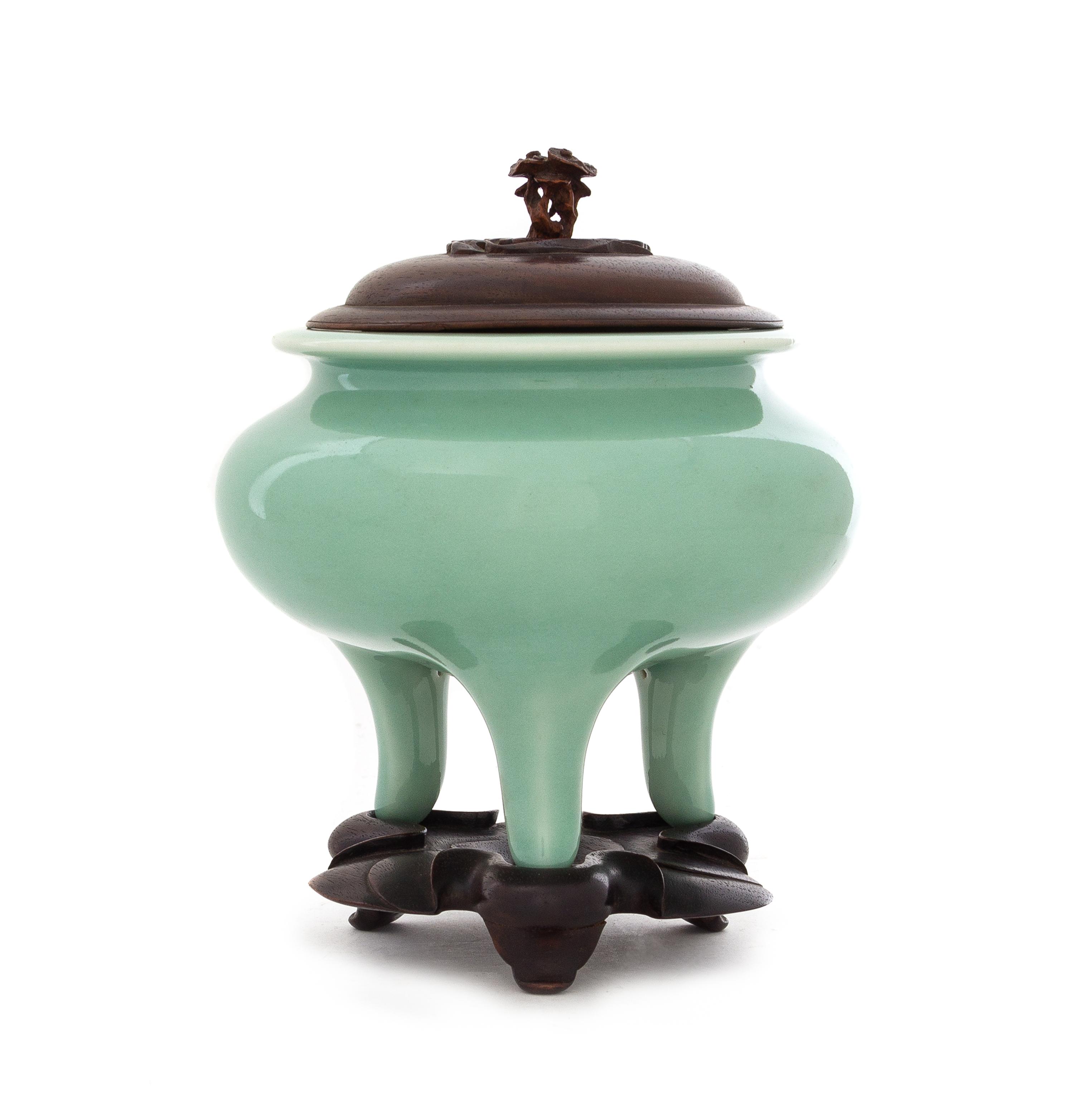 A Japanese Celadon Glazed Porcelain Tripod Incense Burner Height 4 3/4 inches. — PORCELAIN: EARLY 20TH CENTURYWOOD COVER AND STAND: CHINESE, 19TH CENTURY