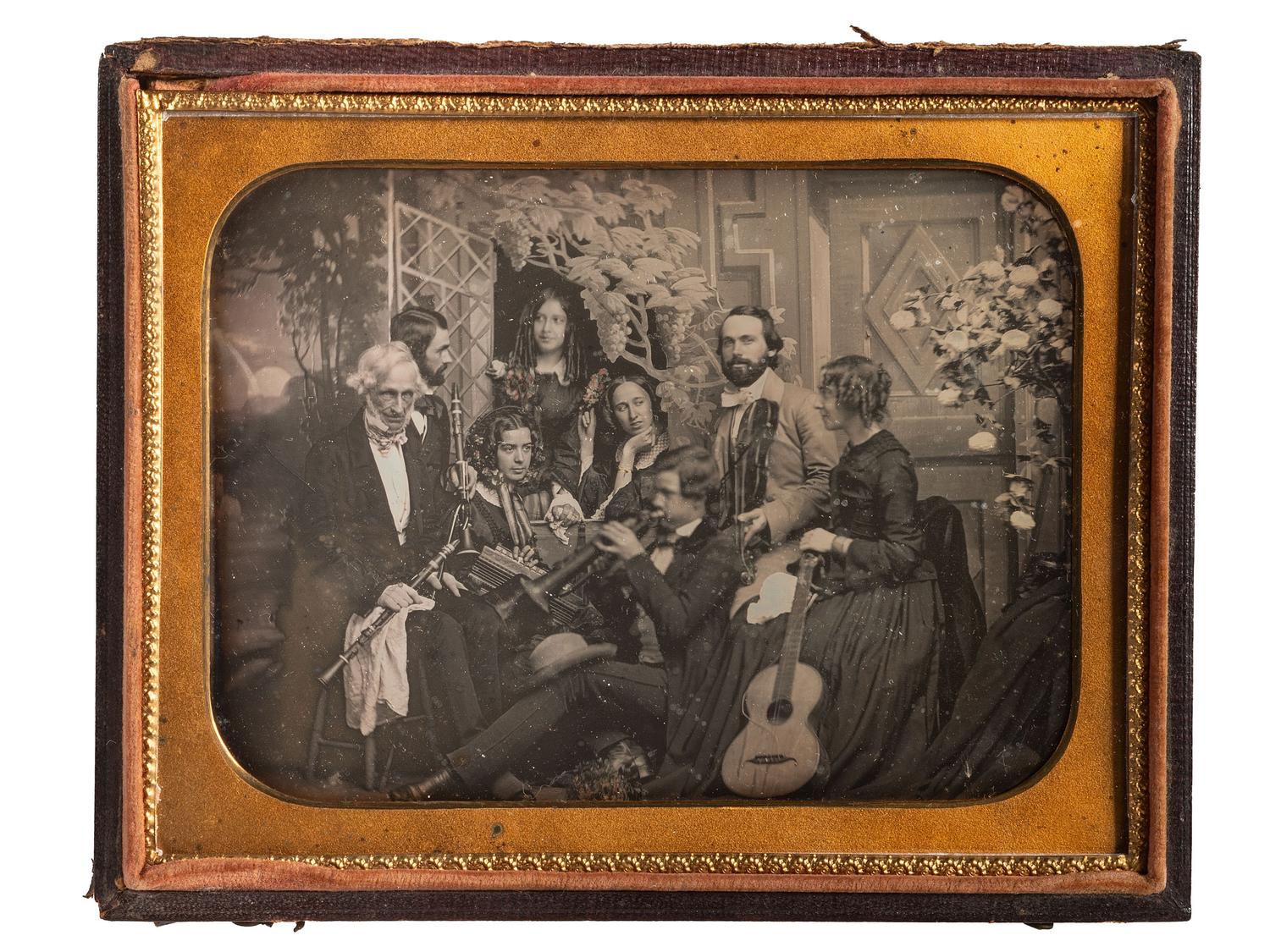 [EARLY PHOTOGRAPHY]. Half plate daguerreotype scene of a group of playful musicians and guests posed together with diverse instruments before a detailed studio backdrop.