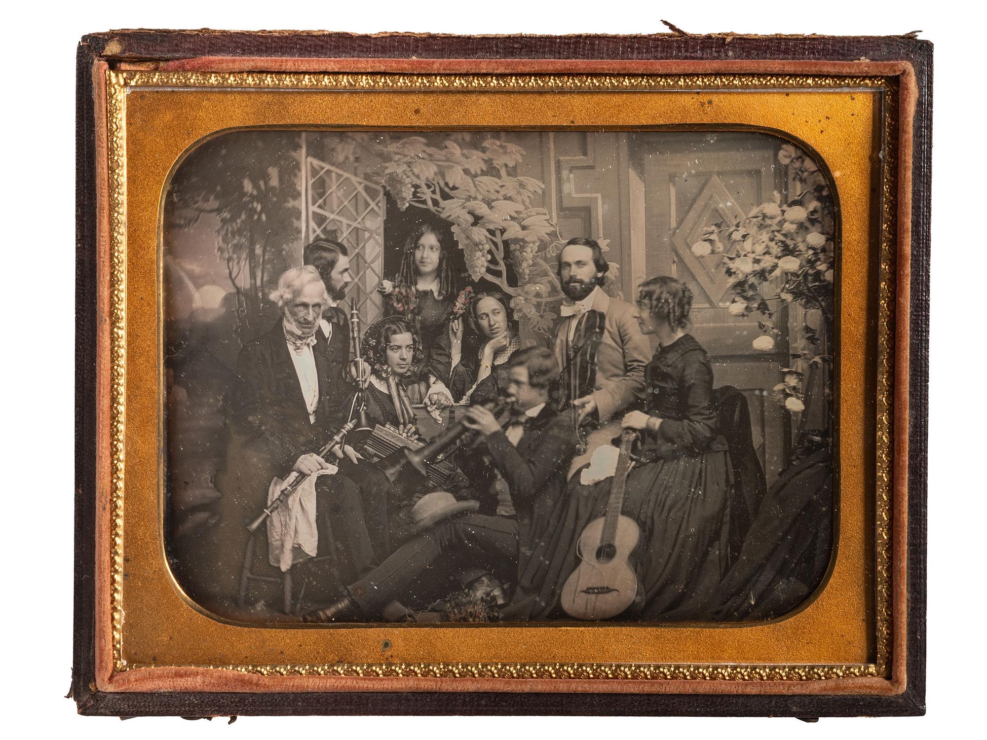 [EARLY PHOTOGRAPHY]. Half plate daguerreotype scene of a group of playful musicians and guests posed together with diverse instruments before a detailed studio backdrop.