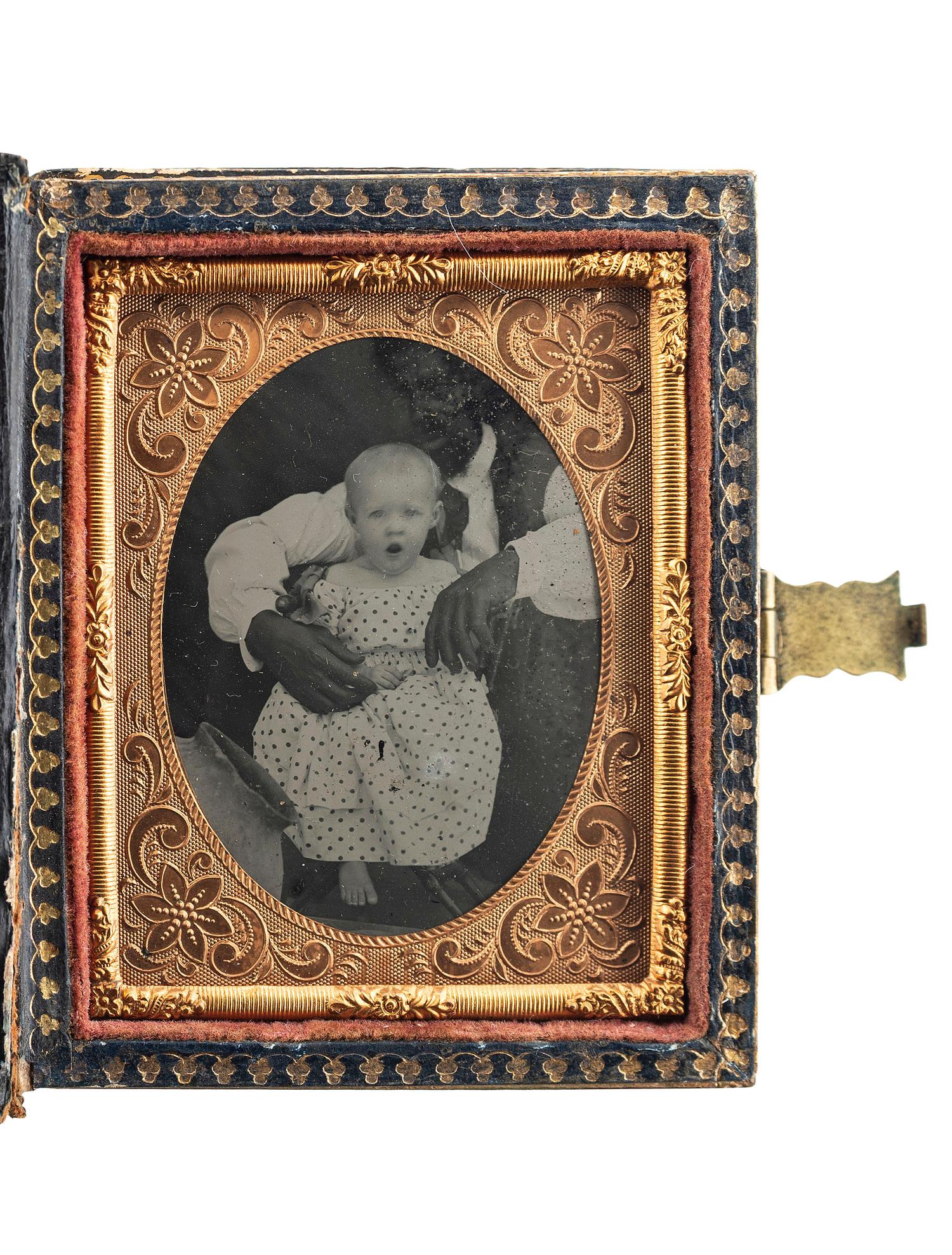 [EARLY PHOTOGRAPHY]. Ninth plate ambrotype of an African American man with white child, with rare Colonoware jar.