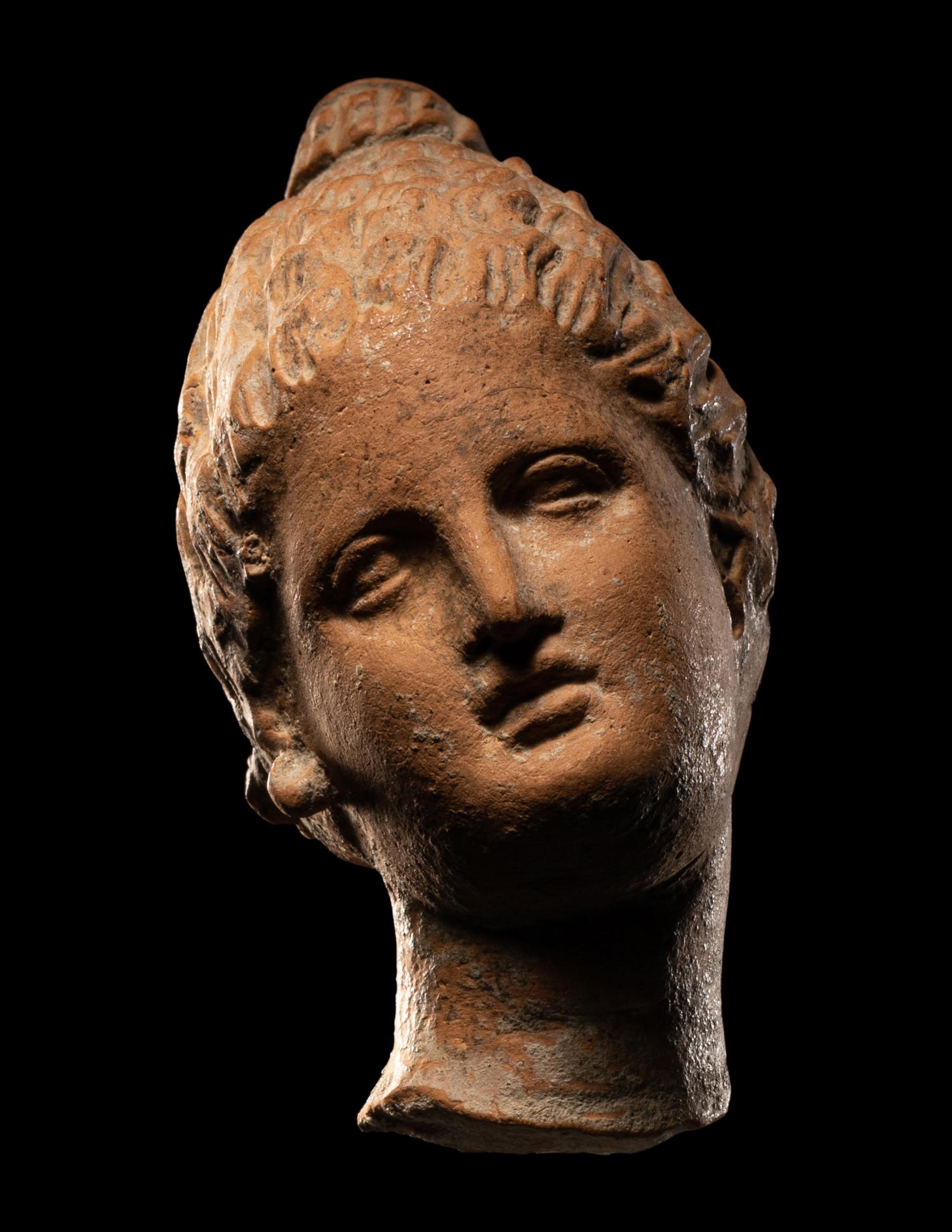 A Greek Terracotta Female Head with Melon Coiffure