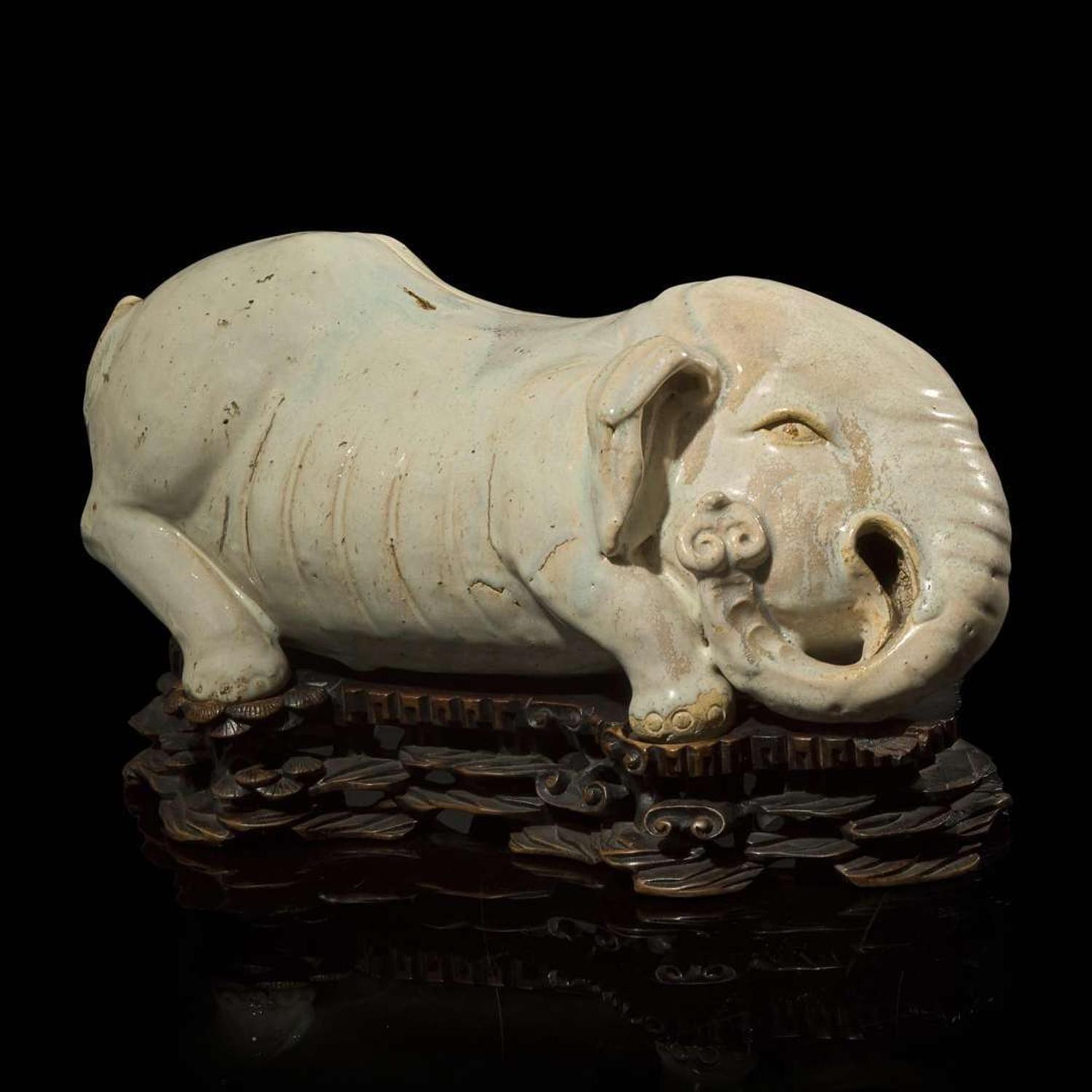 An unusual Chinese elephant-form white-glazed stoneware pillow and carved wood base 白象瓷枕與木座