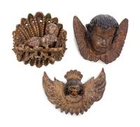 Two Continental Carved and Painted Winged Masks and an Ornament of a Putto Sleeping in a Shell