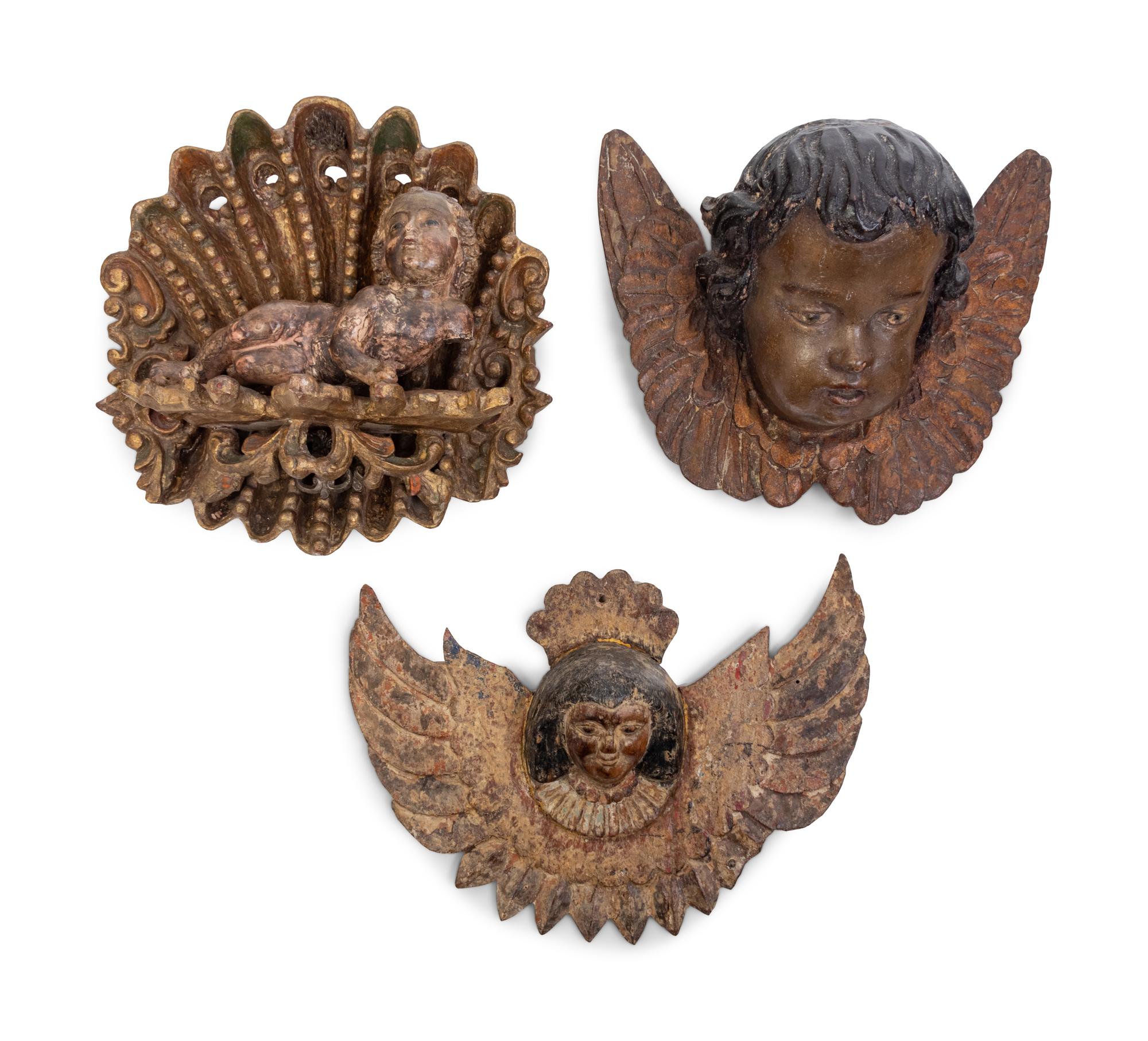 Two Continental Carved and Painted Winged Masks and an Ornament of a Putto Sleeping in a Shell