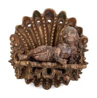 Two Continental Carved and Painted Winged Masks and an Ornament of a Putto Sleeping in a Shell