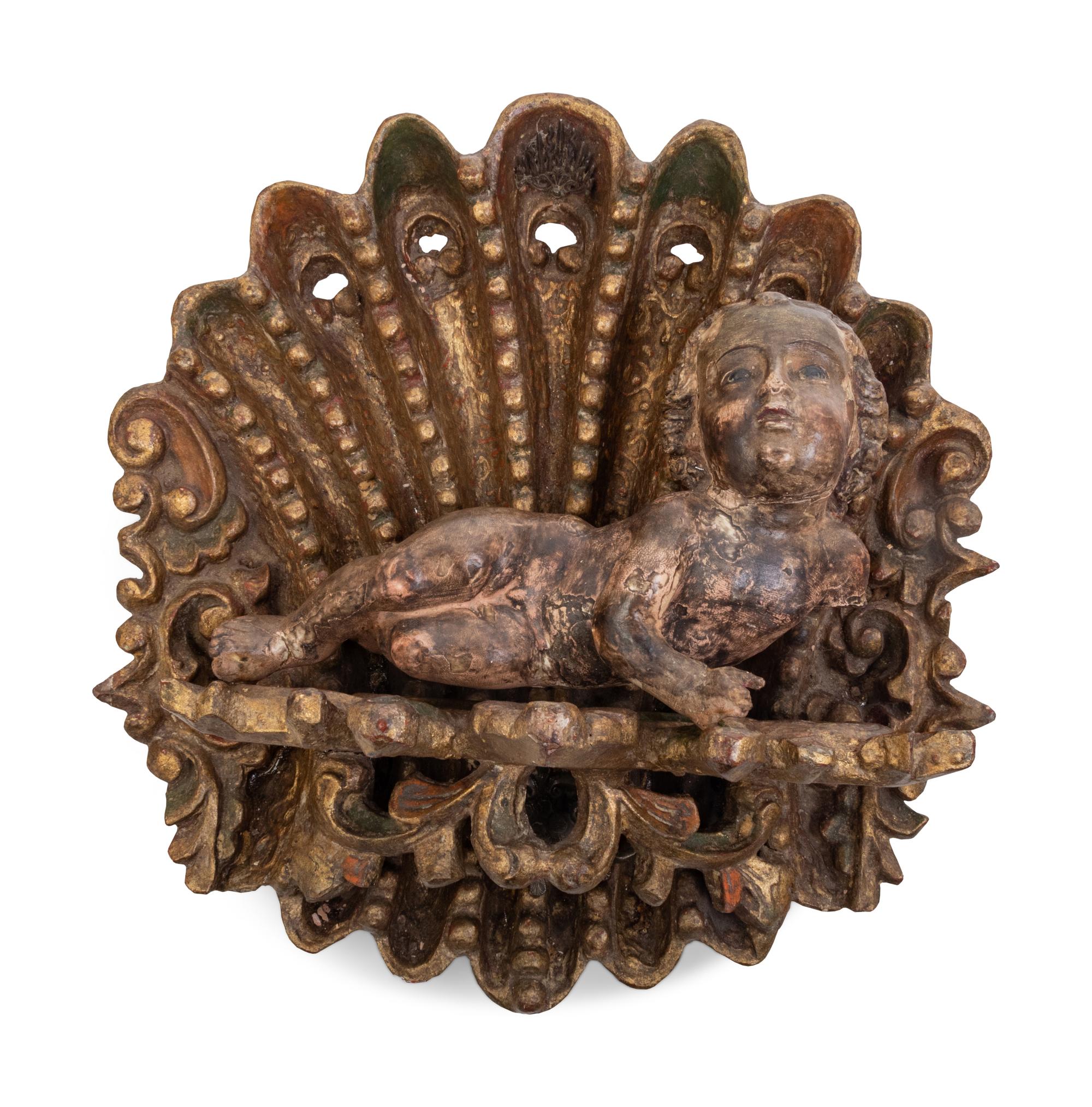 Two Continental Carved and Painted Winged Masks and an Ornament of a Putto Sleeping in a Shell