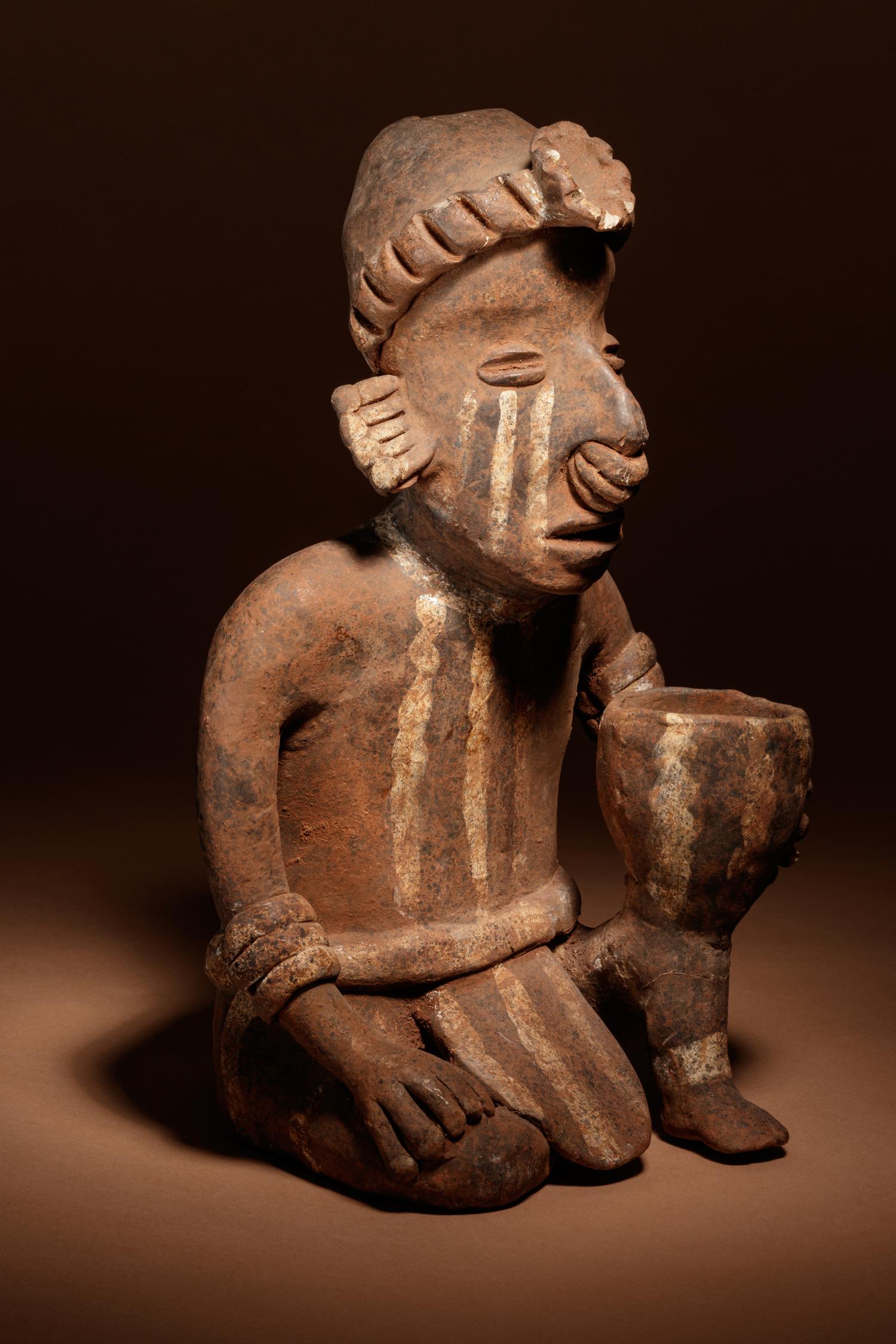 A Nayarit Terracotta Crouching Figure with Vessel