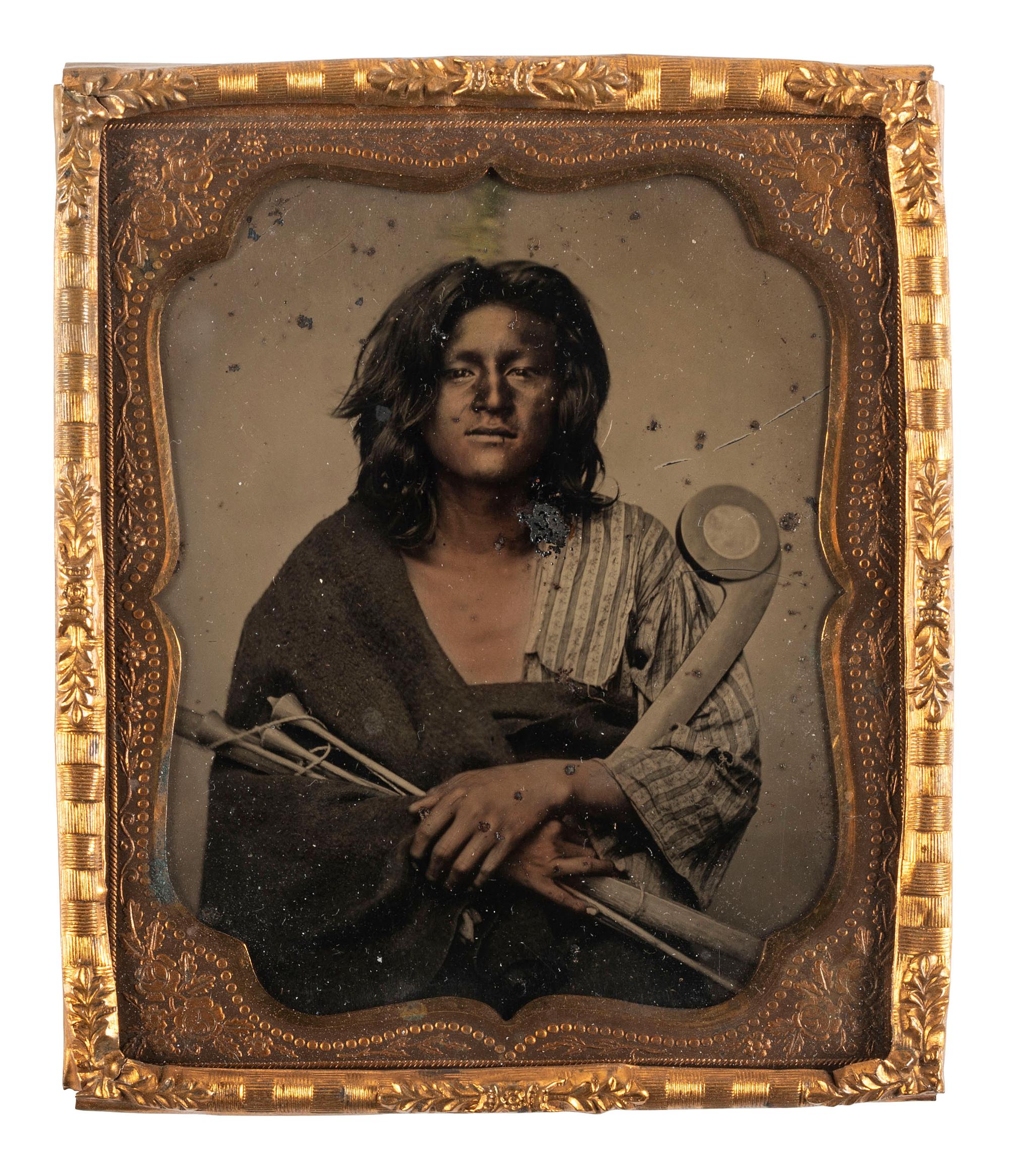 [NATIVE AMERICANS]. Sixth plate tintype of a young Native American man, likely Winnebago, posed with a war club and bird arrows. Ca 1865.