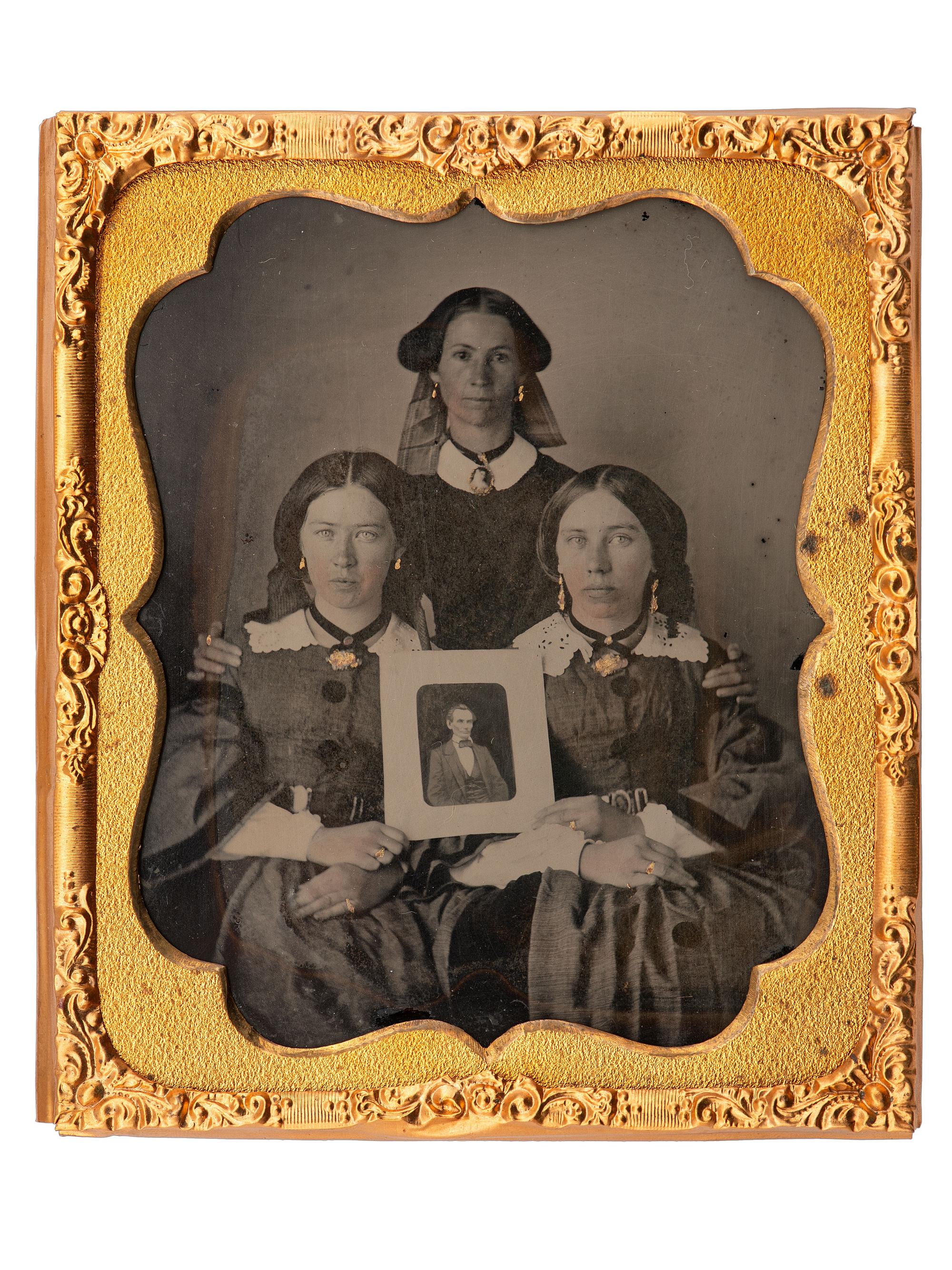 [LINCOLNIANA - EARLY PHOTOGRAPHY]. Sixth plate ambrotype of three patriotic women proudly displaying a portrait of Abraham Lincoln.