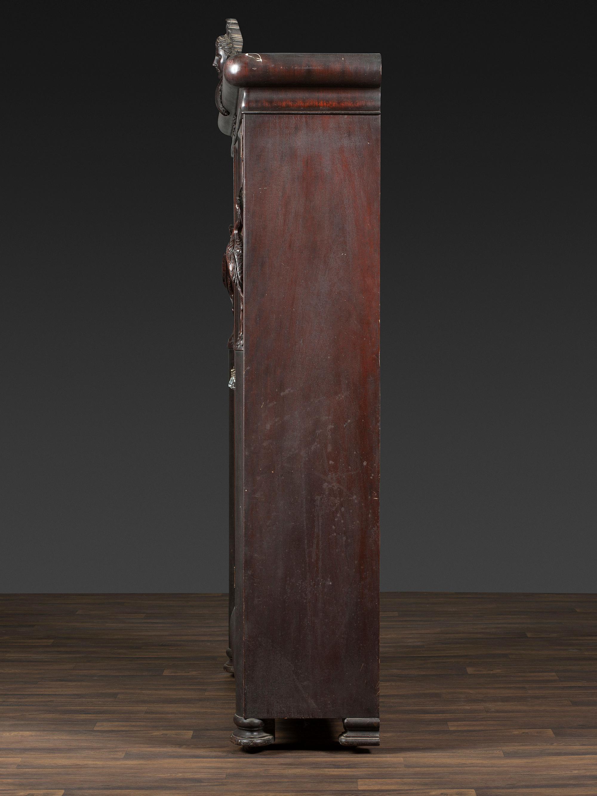 An Aesthetic Movement Crane and Mask Carved Mahogany and Glass Paneled Bookcase