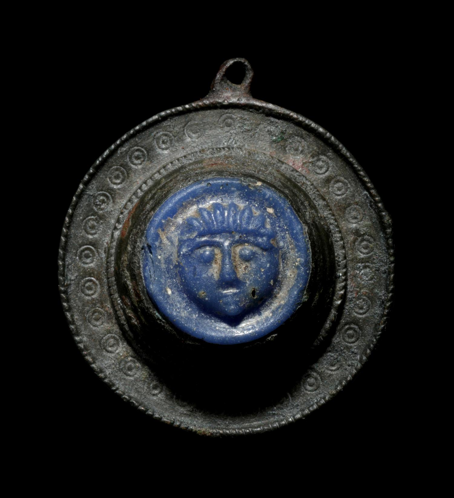 A Romano-Celtic Bronze and Blue Glass Fibula with a Mask