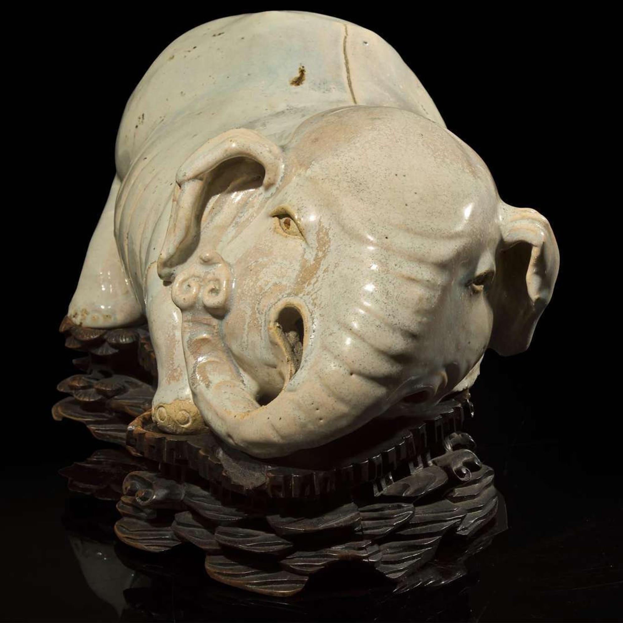 An unusual Chinese elephant-form white-glazed stoneware pillow and carved wood base 白象瓷枕與木座