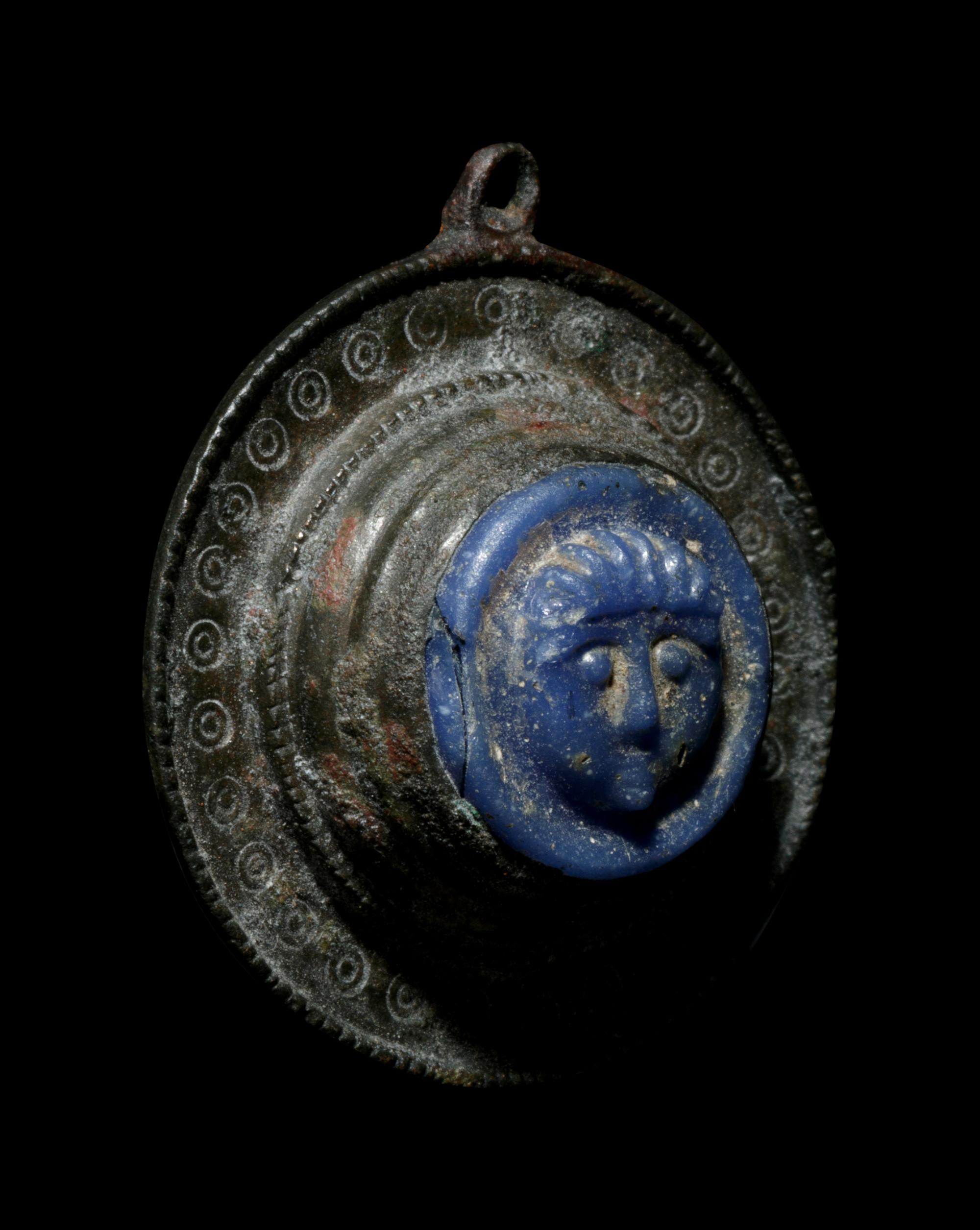 A Romano-Celtic Bronze and Blue Glass Fibula with a Mask