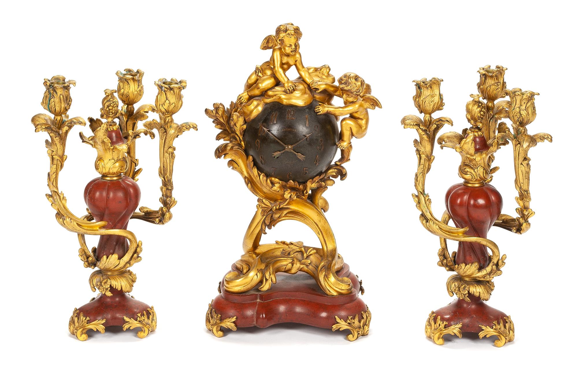 A French Gilt Bronze and Rouge Marble Clock Garniture Height of mantel clock 19 inches; height of candelabra 15 inches. — 19TH CENTURY