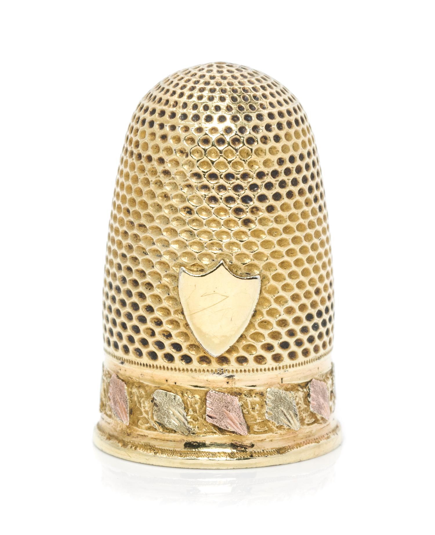 A Continental Tri-Color Gold Thimble, , the knurled domed top and body above a rose and white gold band of continuous foliate decoratio