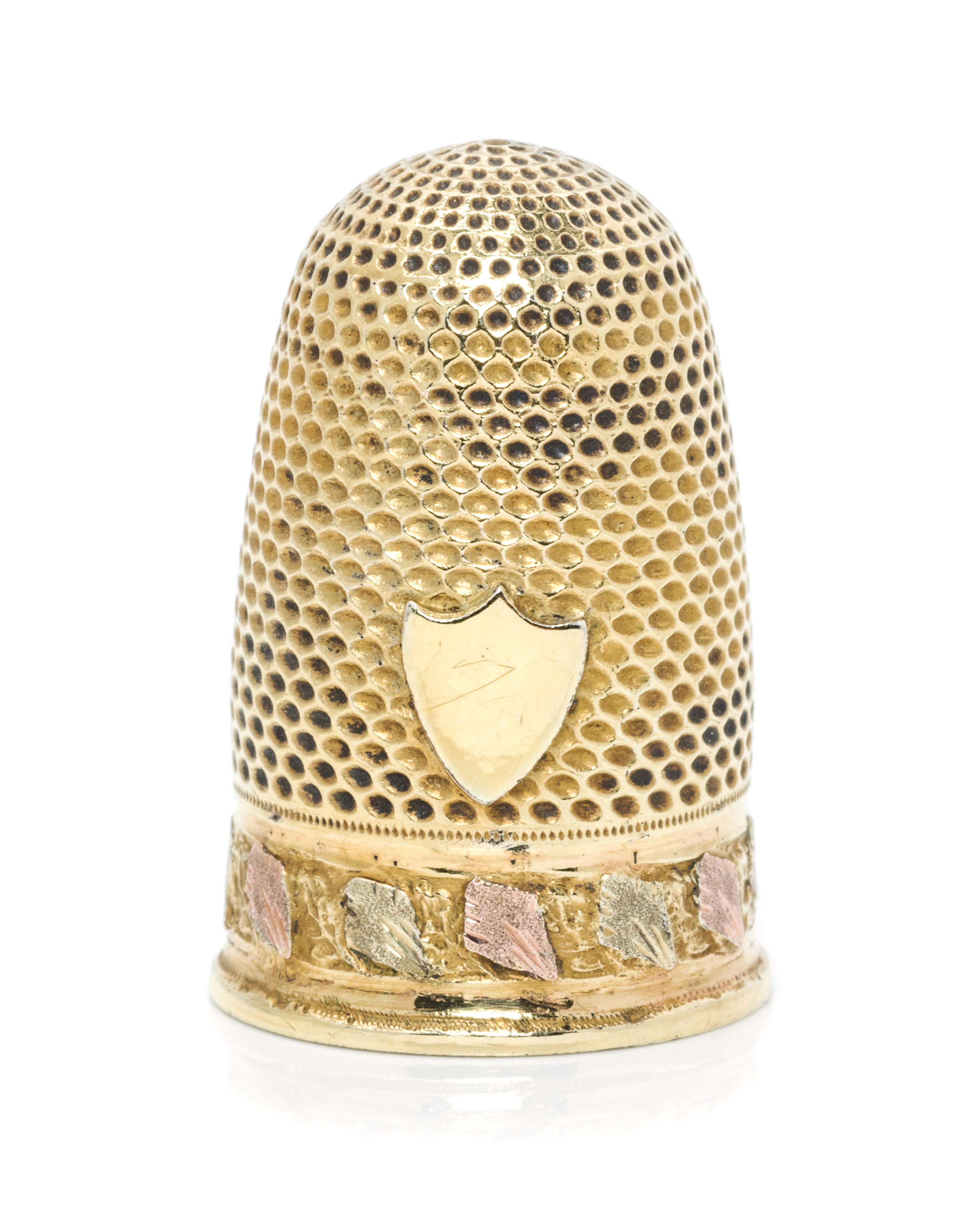 A Continental Tri-Color Gold Thimble, , the knurled domed top and body above a rose and white gold band of continuous foliate decoratio