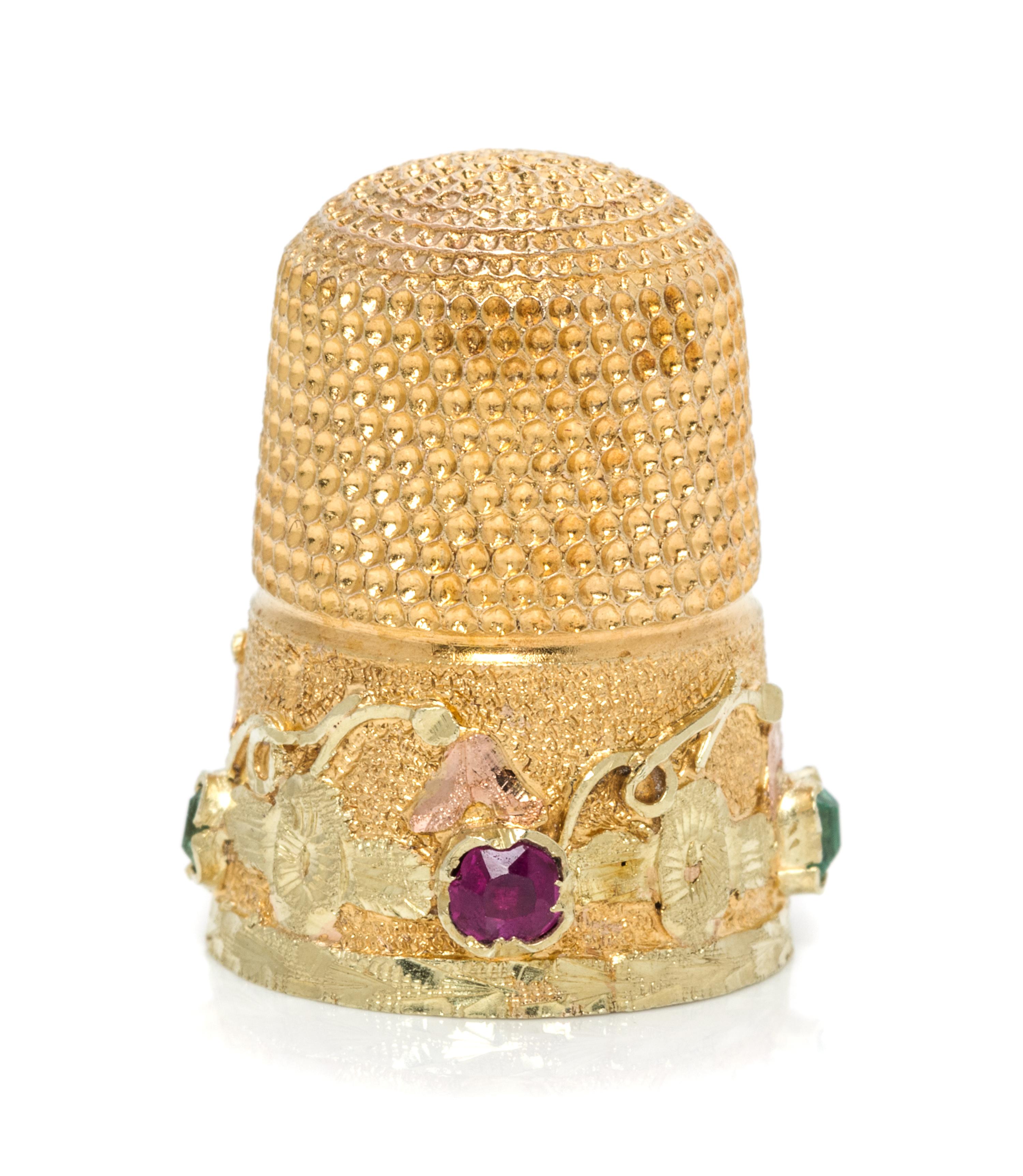 An American Gold and Gemstone Thimble, , the knurled top and body above a floral and foliate band inset with two rubies and two green b
