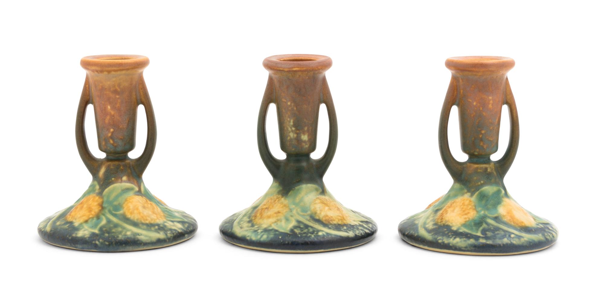 A Set of Three Roseville Sunflower Pottery Candlesticks Height of each 4 1/4 inches.