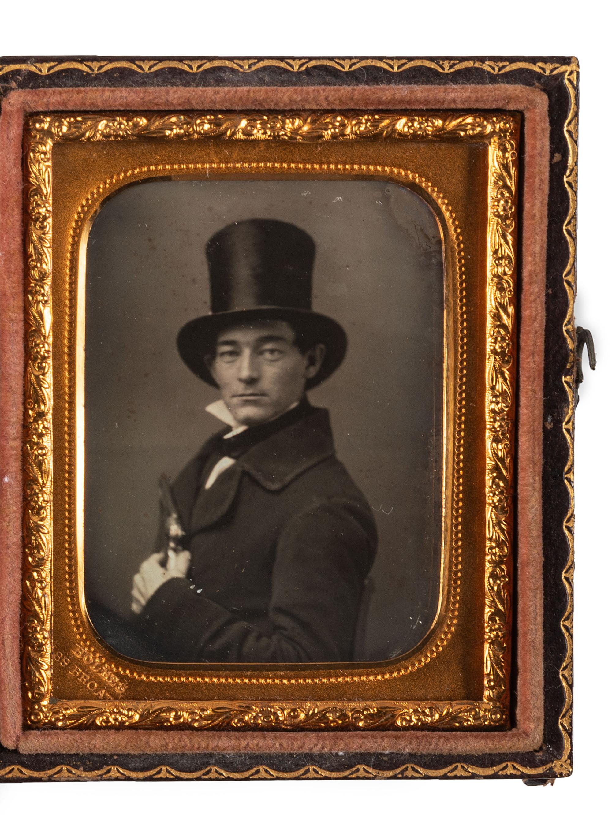 [EARLY PHOTOGRAPHY]. Ninth plate daguerreotype portrait of a man wearing a top hat and holding a revolver to his chest. New York: Holmes, n.d.
