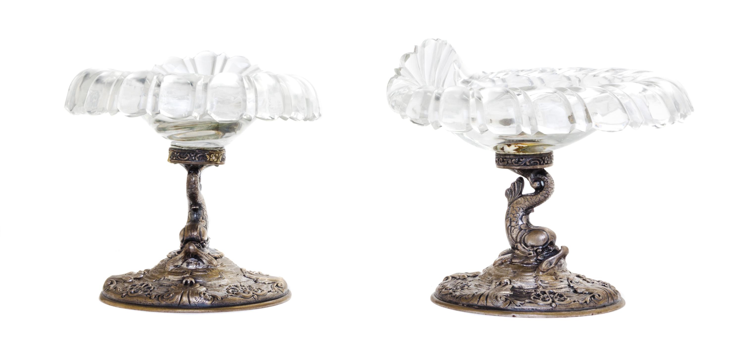 A Pair of German Silver and Glass Compotes, First Half 20th Century, having etched glass shell form bowls raised on dolphin form suppor