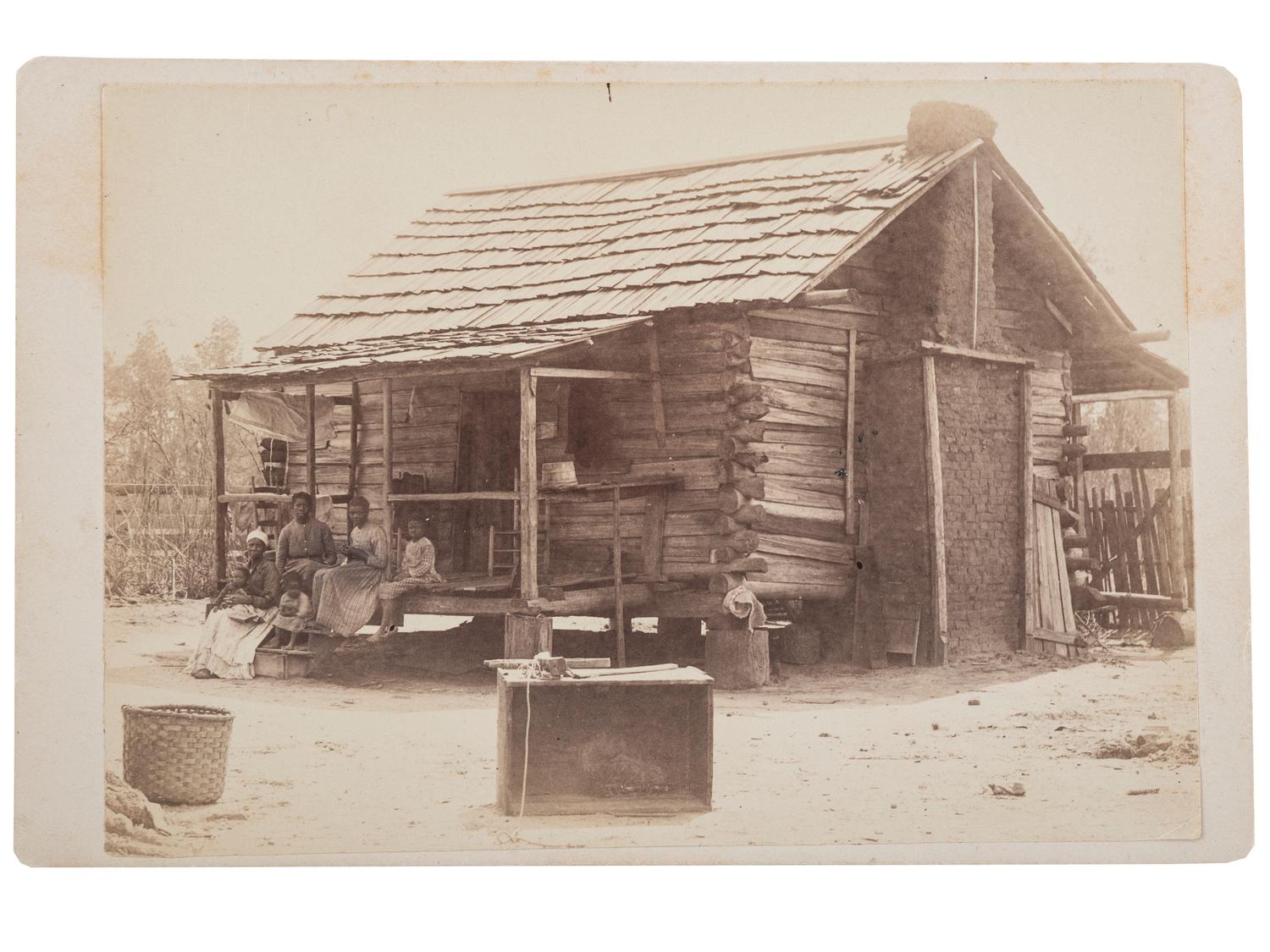 [EARLY PHOTOGRAPHY]. A group of 2 cabinet photographs of African American families posing in front of log cabins. Ca 1890s.