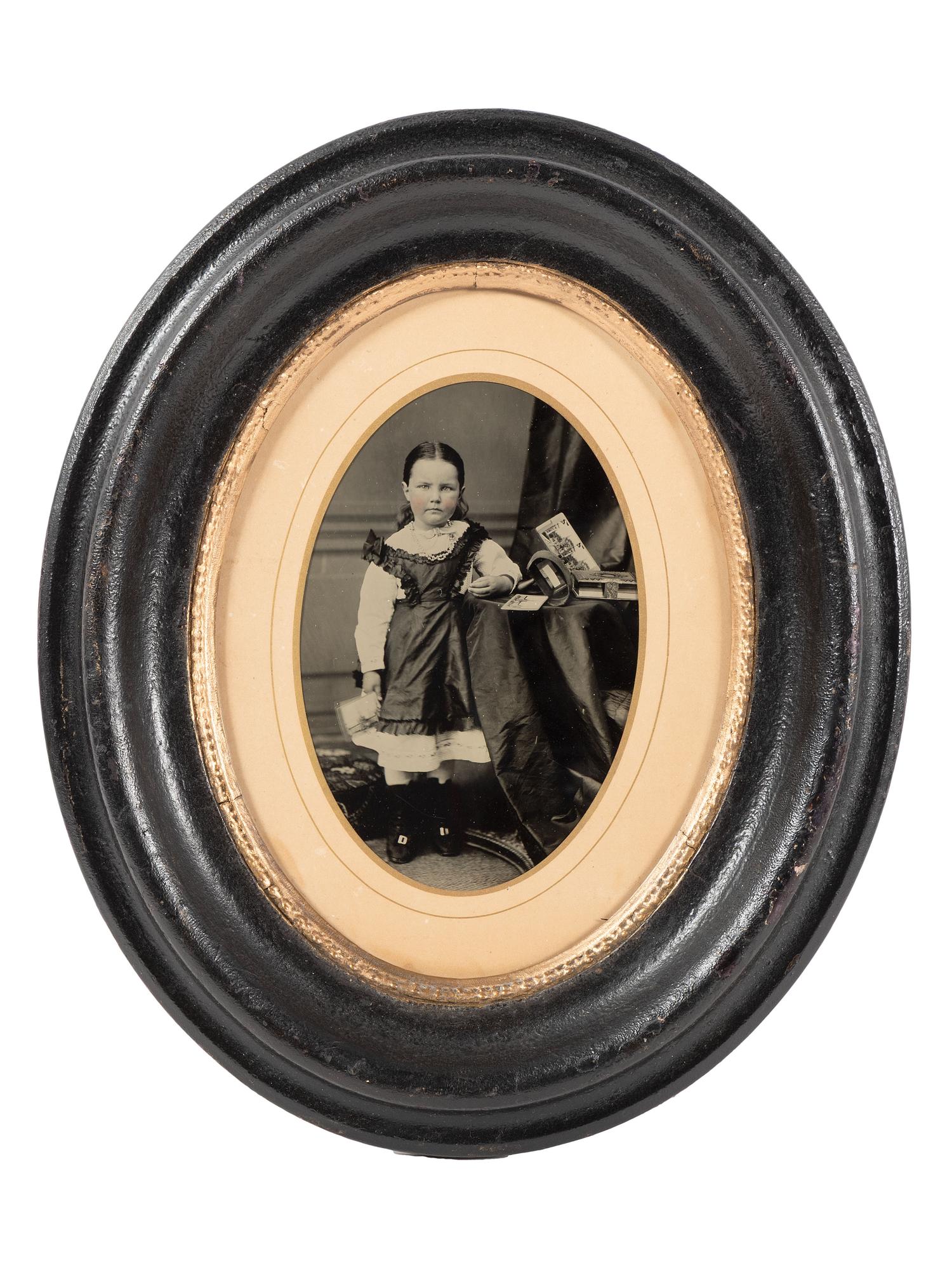 [EARLY PHOTOGRAPHY]. Tintype portrait of a little girl posed with stereoviews, viewer, and photo album.