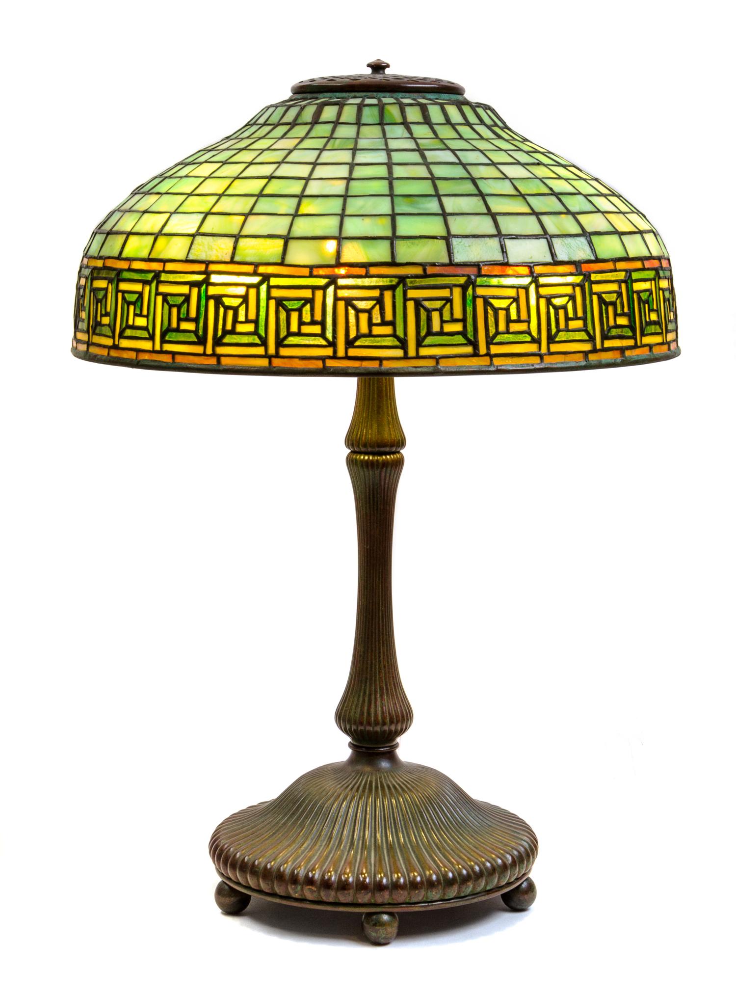 A Tiffany Studios Leaded Favrile Glass and Bronze Greek Key Table Lamp Height 23 x diameter of shade 16 inches.