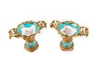 A Pair of Sèvres Style Gilt Bronze Mounted Painted and Parcel Gilt Porcelain Tazze