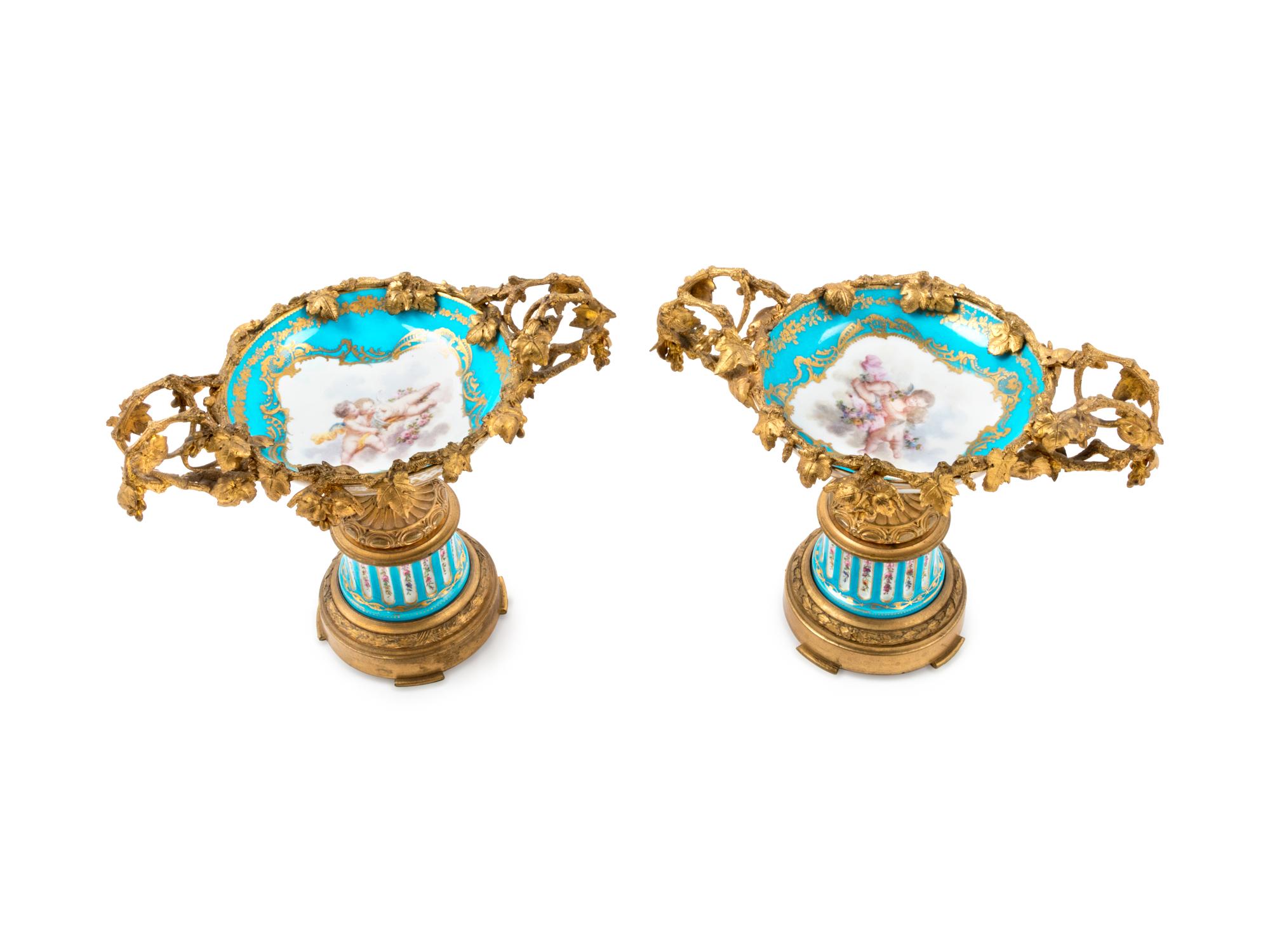 A Pair of Sèvres Style Gilt Bronze Mounted Painted and Parcel Gilt Porcelain Tazze