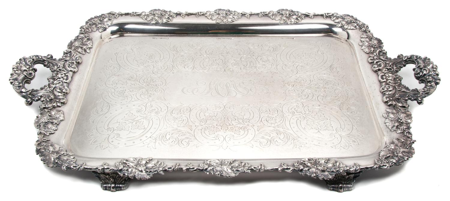 An English Silver-Plate Handled Tray, , having C-scroll handles, with grapevine border centered with a monogram, raised on feet.