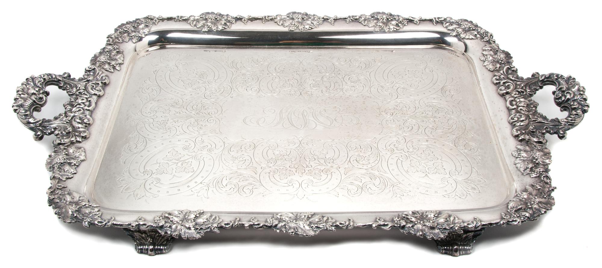 An English Silver-Plate Handled Tray, , having C-scroll handles, with grapevine border centered with a monogram, raised on feet.