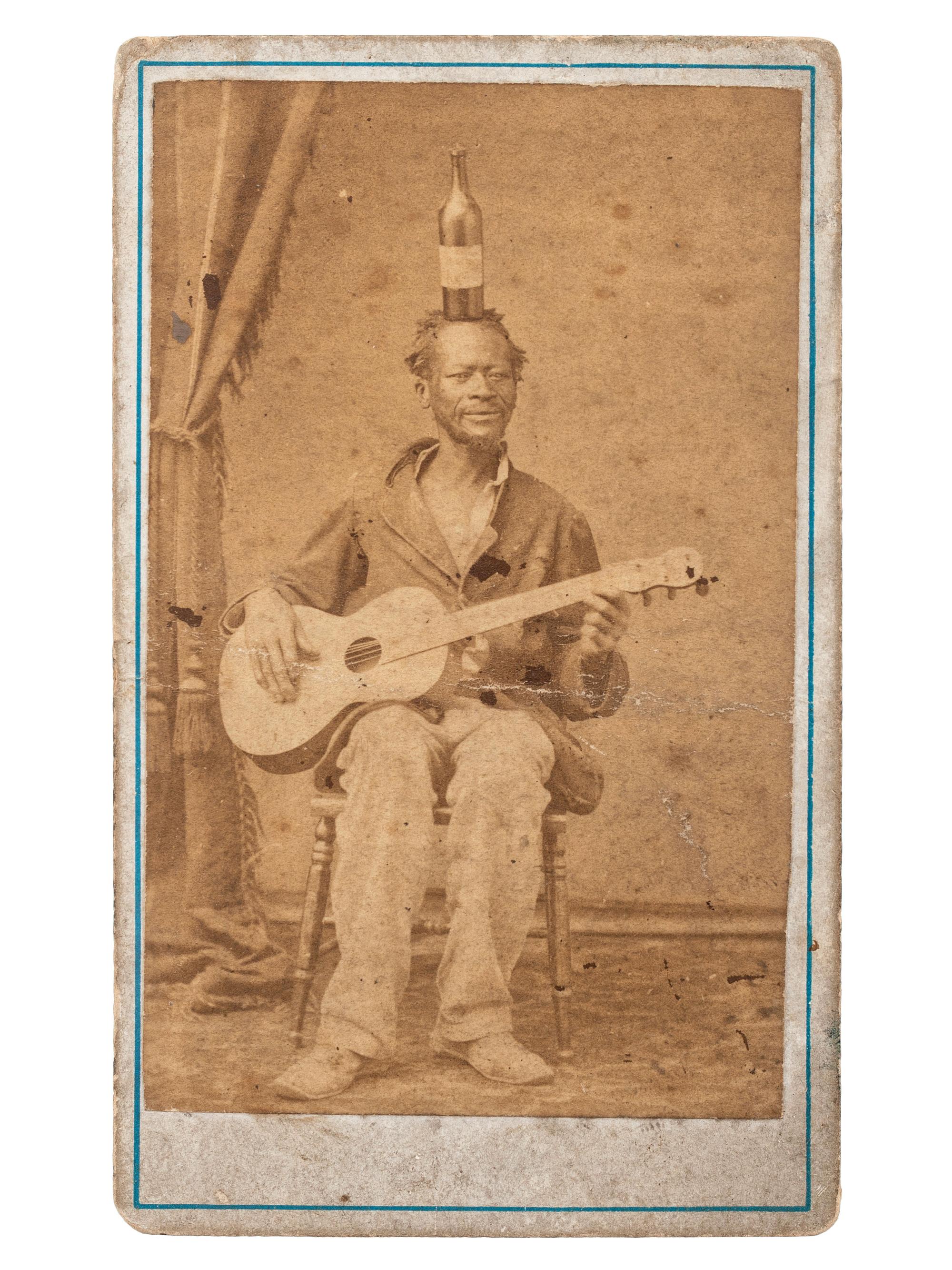 [EARLY PHOTOGRAPHY]. CDV of an African American guitarist balancing a bottle on his head. Ca 1860s.