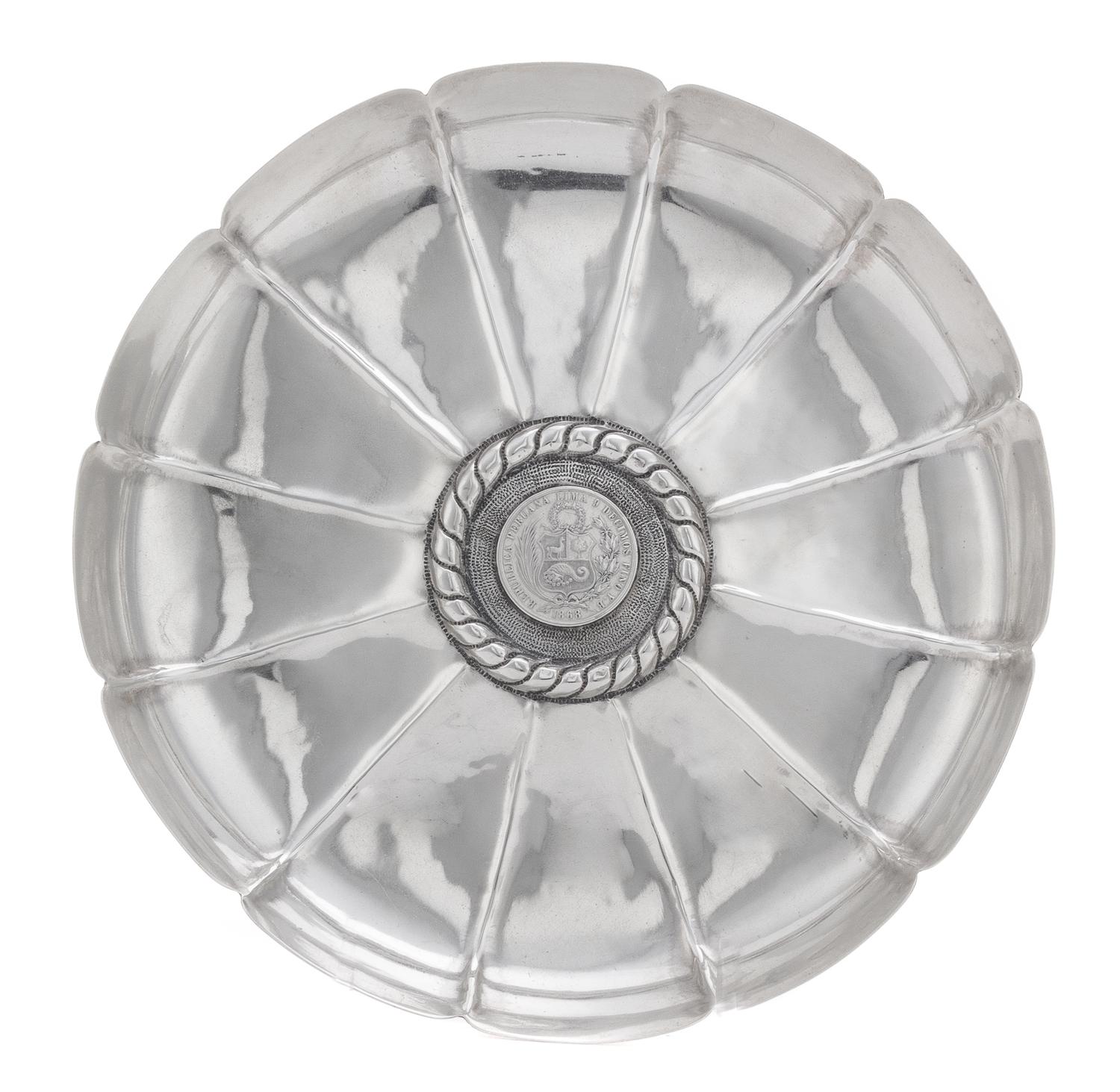 A Peruvian Silver Dish, , having a scalloped edge and a ribbed interior, centered by a banded motif surrounding an 1868 1 sol silver co