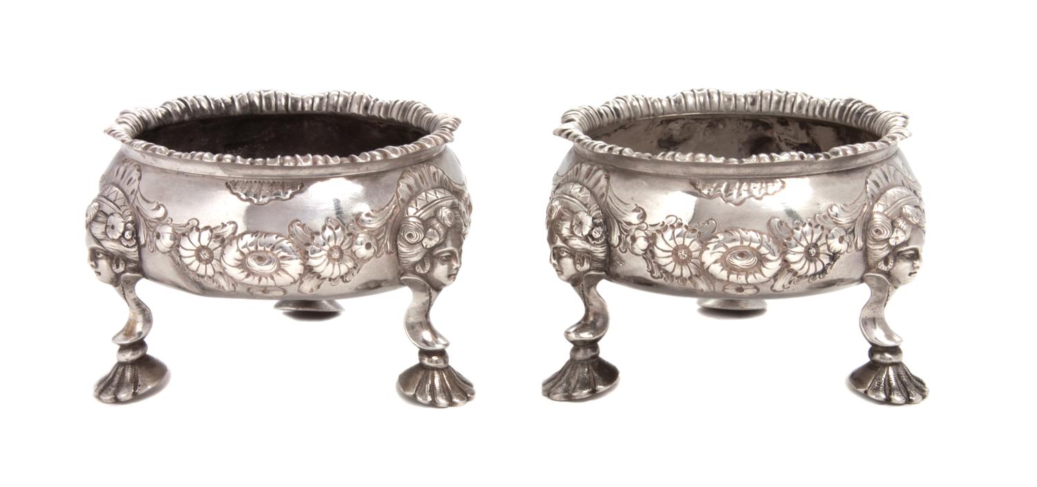 A Pair of English Silver Salts, London, each chased with flower heads and shellwork, raised on three feet headed by masks and ending in