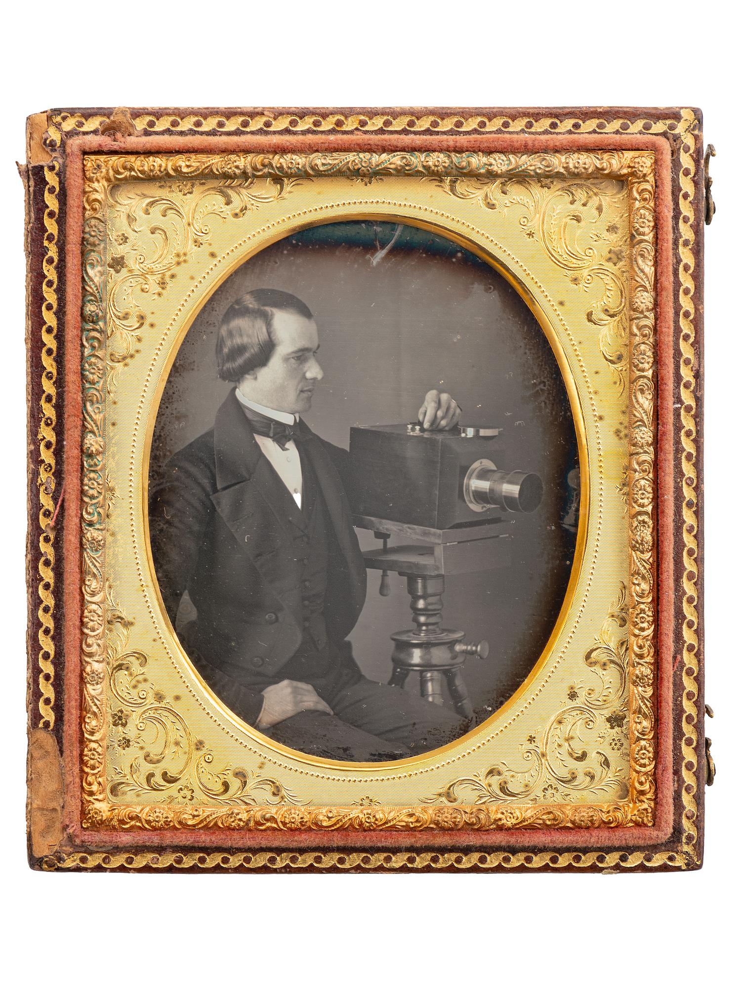 [EARLY PHOTOGRAPHY]. Sixth plate daguerreotype of a photographer posed with an American-made chamfered box camera atop a wooden tripod.