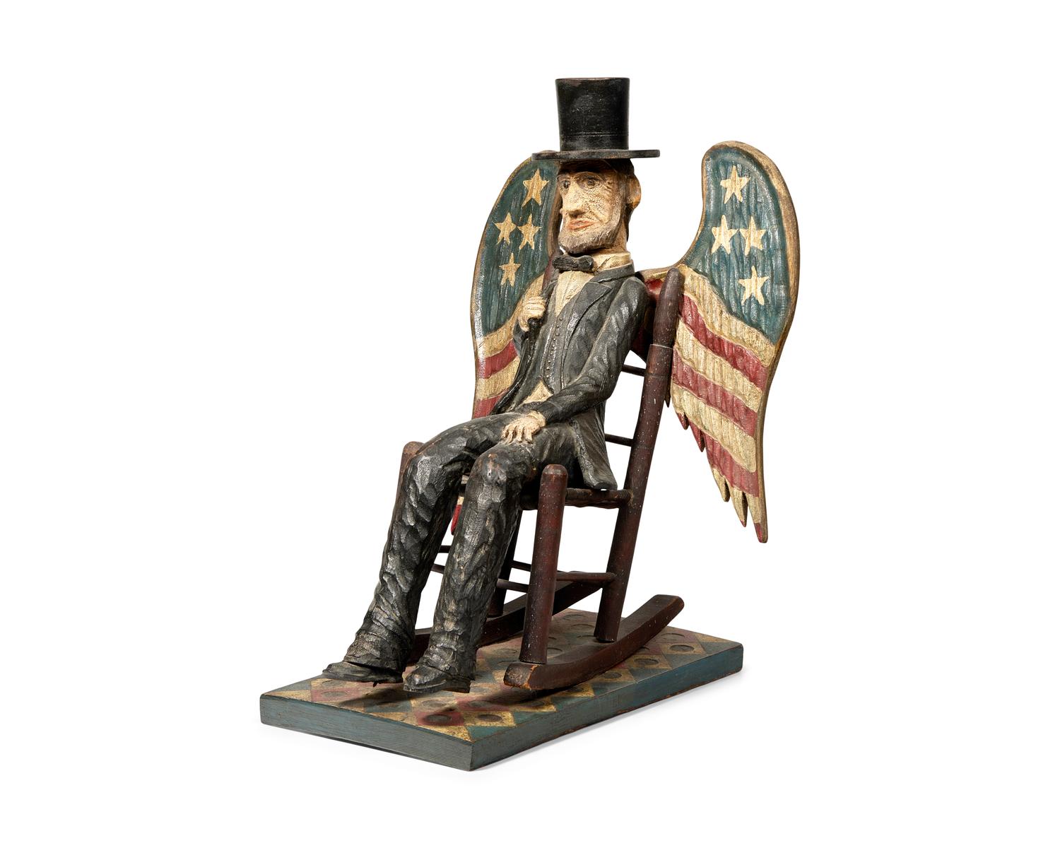 A Carved And Painted Figure Of A Seated Abraham Lincoln With Wings Painted As American Flag