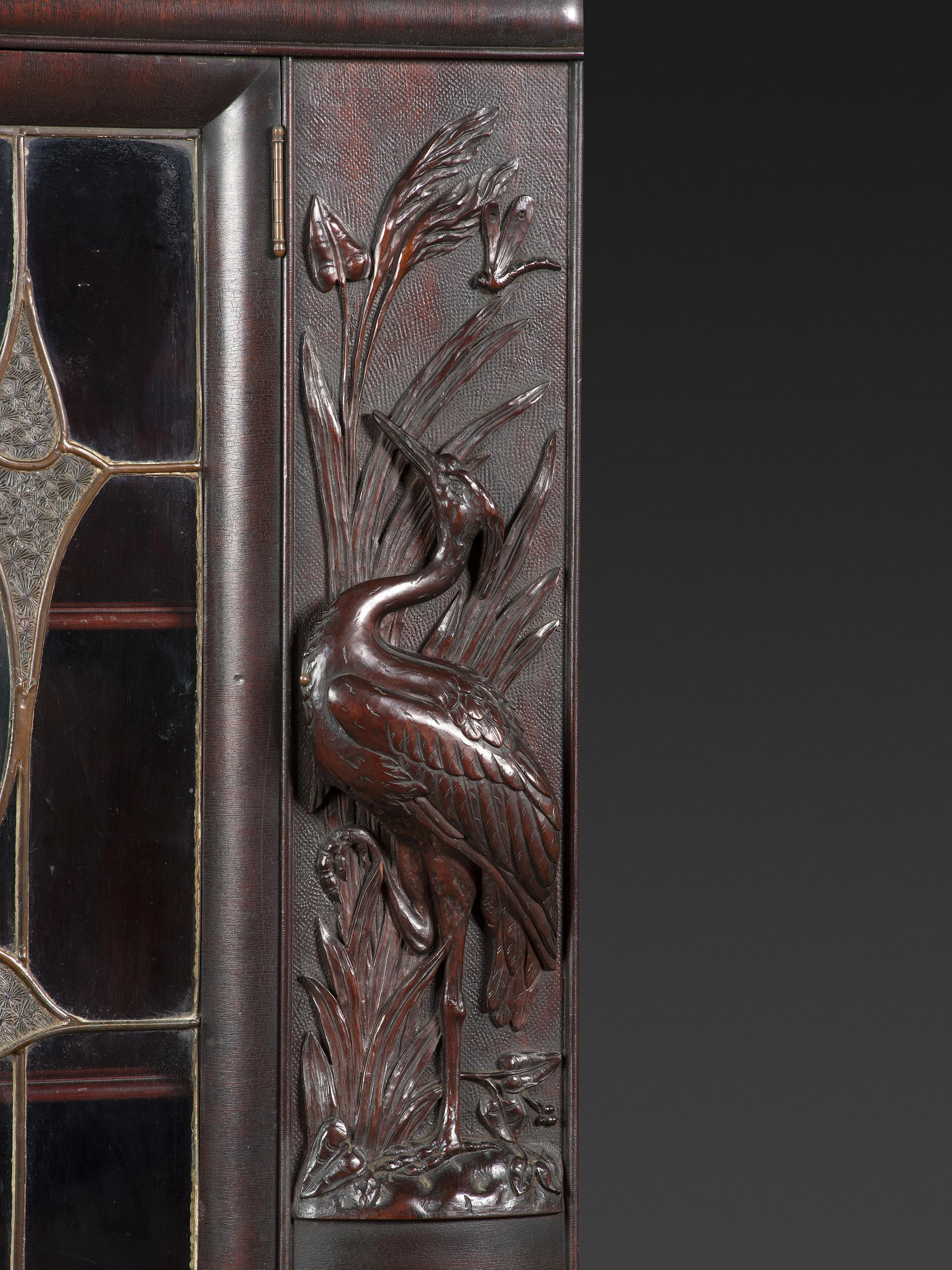 An Aesthetic Movement Crane and Mask Carved Mahogany and Glass Paneled Bookcase