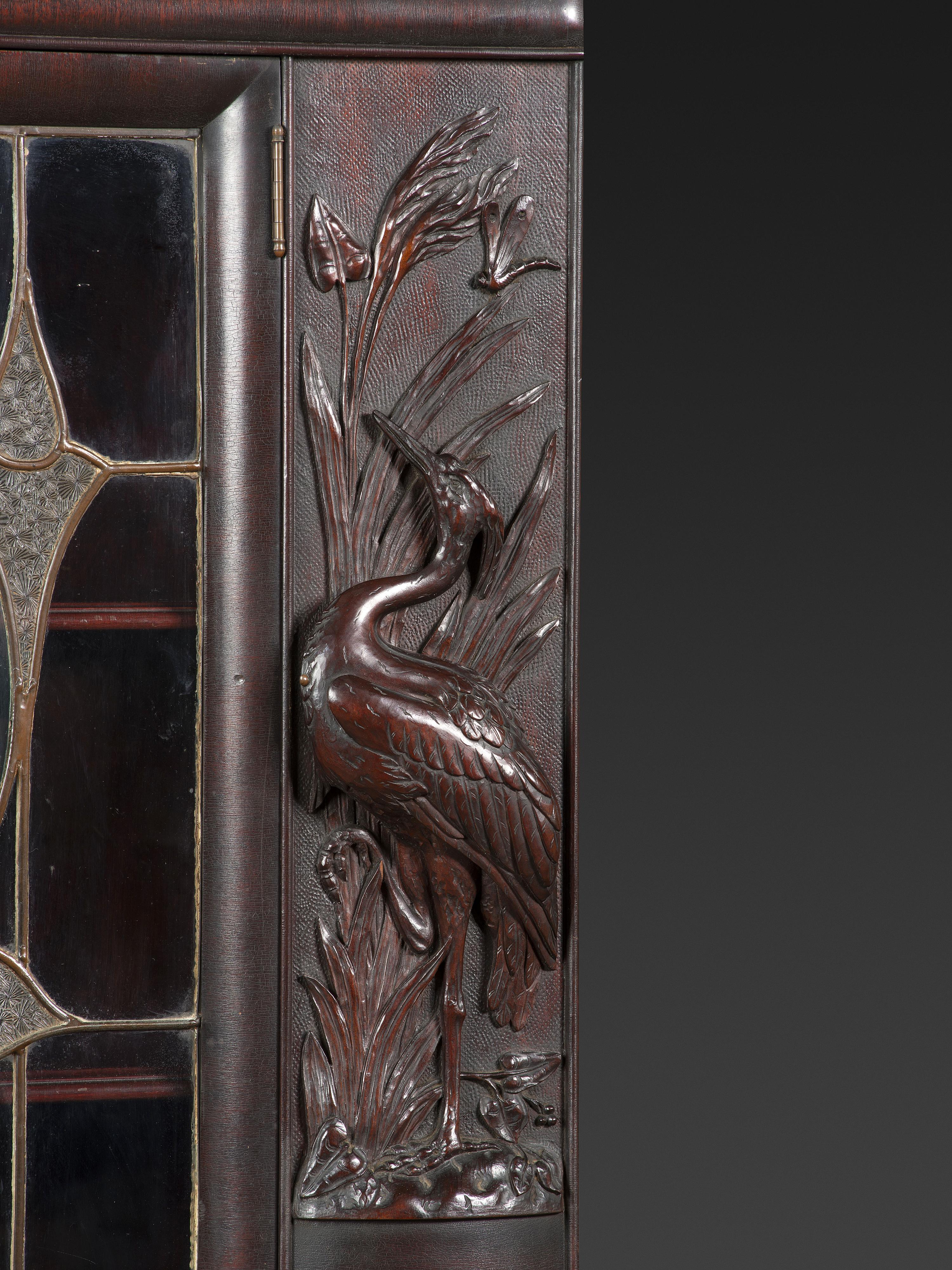 An Aesthetic Movement Crane and Mask Carved Mahogany and Glass Paneled Bookcase