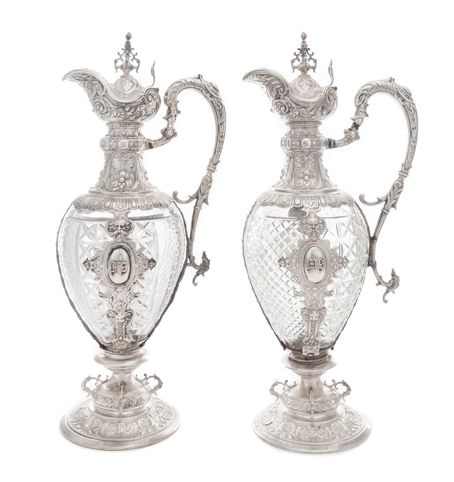 A Pair of Continental Silver Mounted Cut Glass Claret Jugs, Likely German, 19th Century, each having an urn finial above the hinged lid