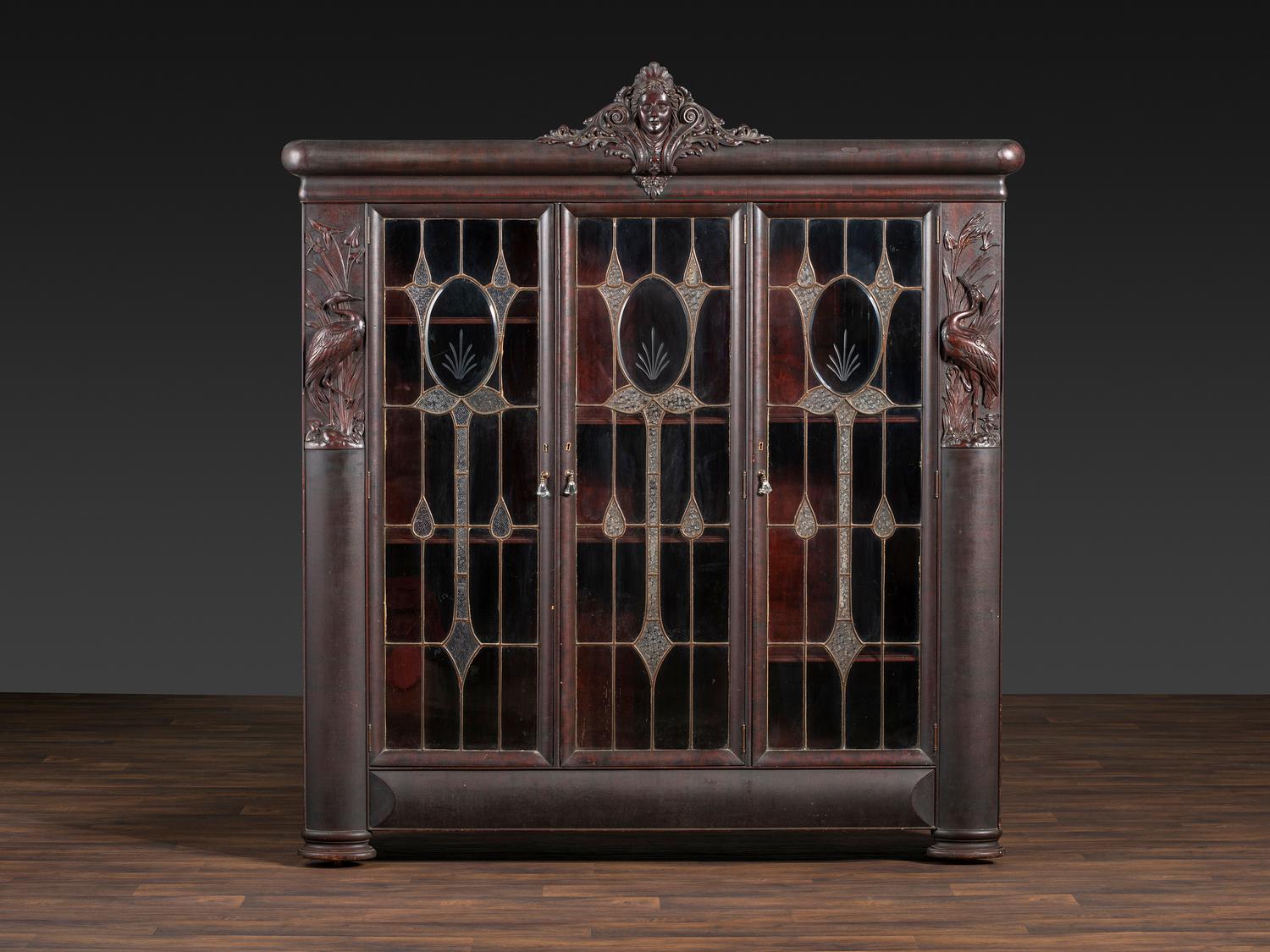 An Aesthetic Movement Crane and Mask Carved Mahogany and Glass Paneled Bookcase