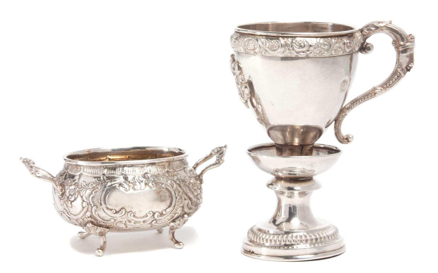 Two German Silver Table Articles, , the first a handled cup raised on pedestal, having a foliate border and vacant emblematic crest, ma