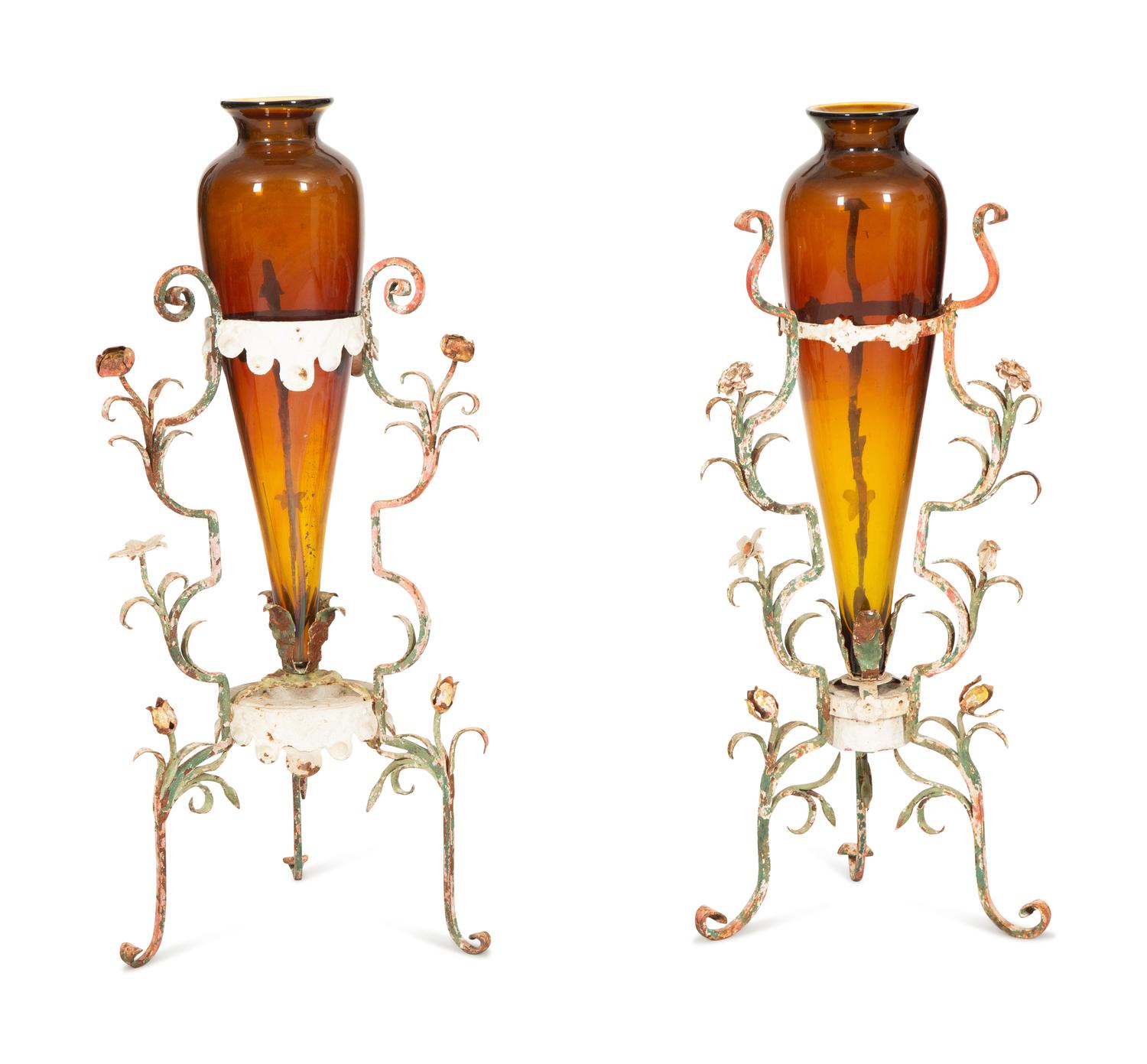 A Pair of Polychrome Painted Metal Stands with Amber Glass Amphora Vases