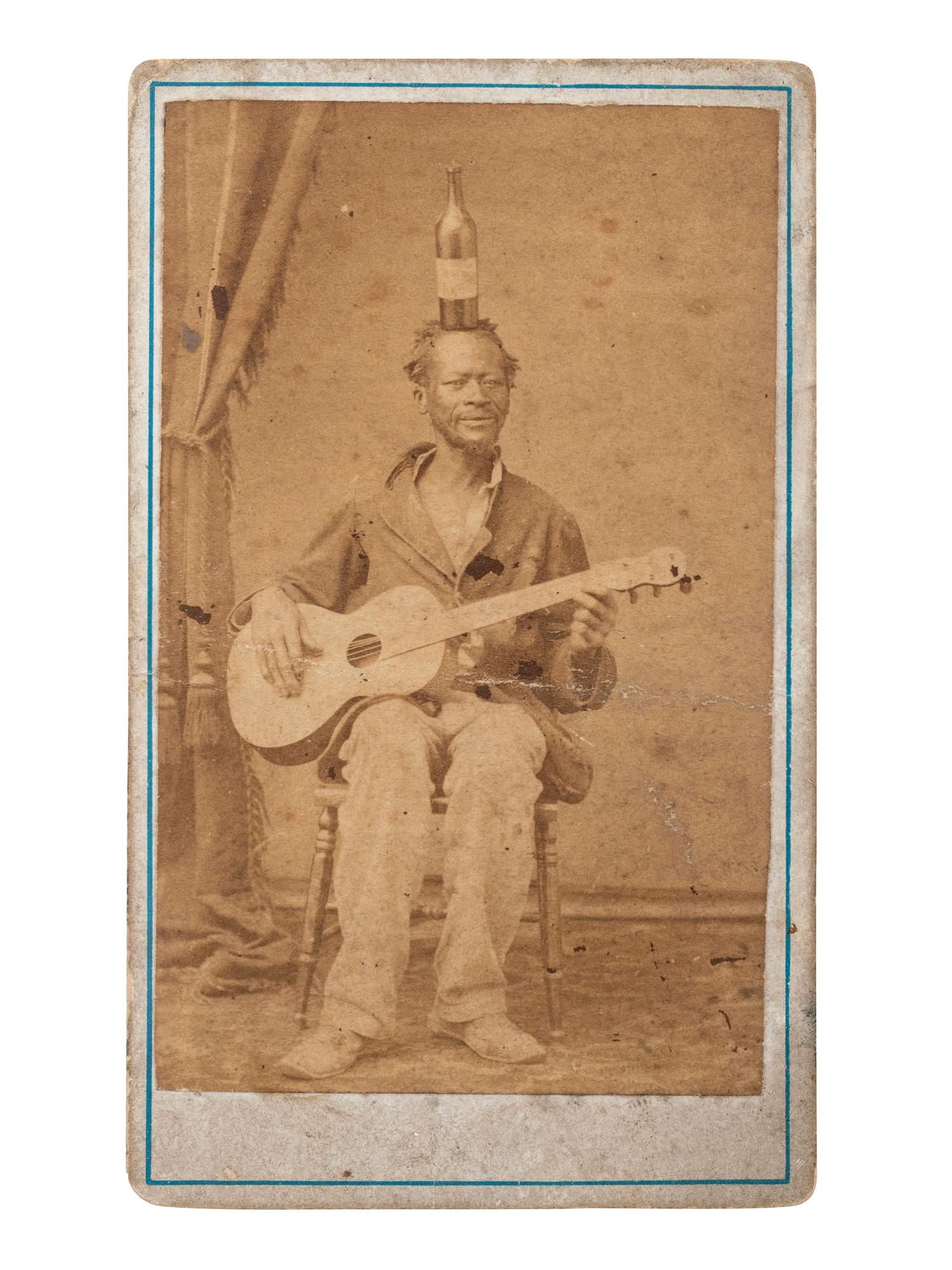 [EARLY PHOTOGRAPHY]. CDV of an African American guitarist balancing a bottle on his head. Ca 1860s.