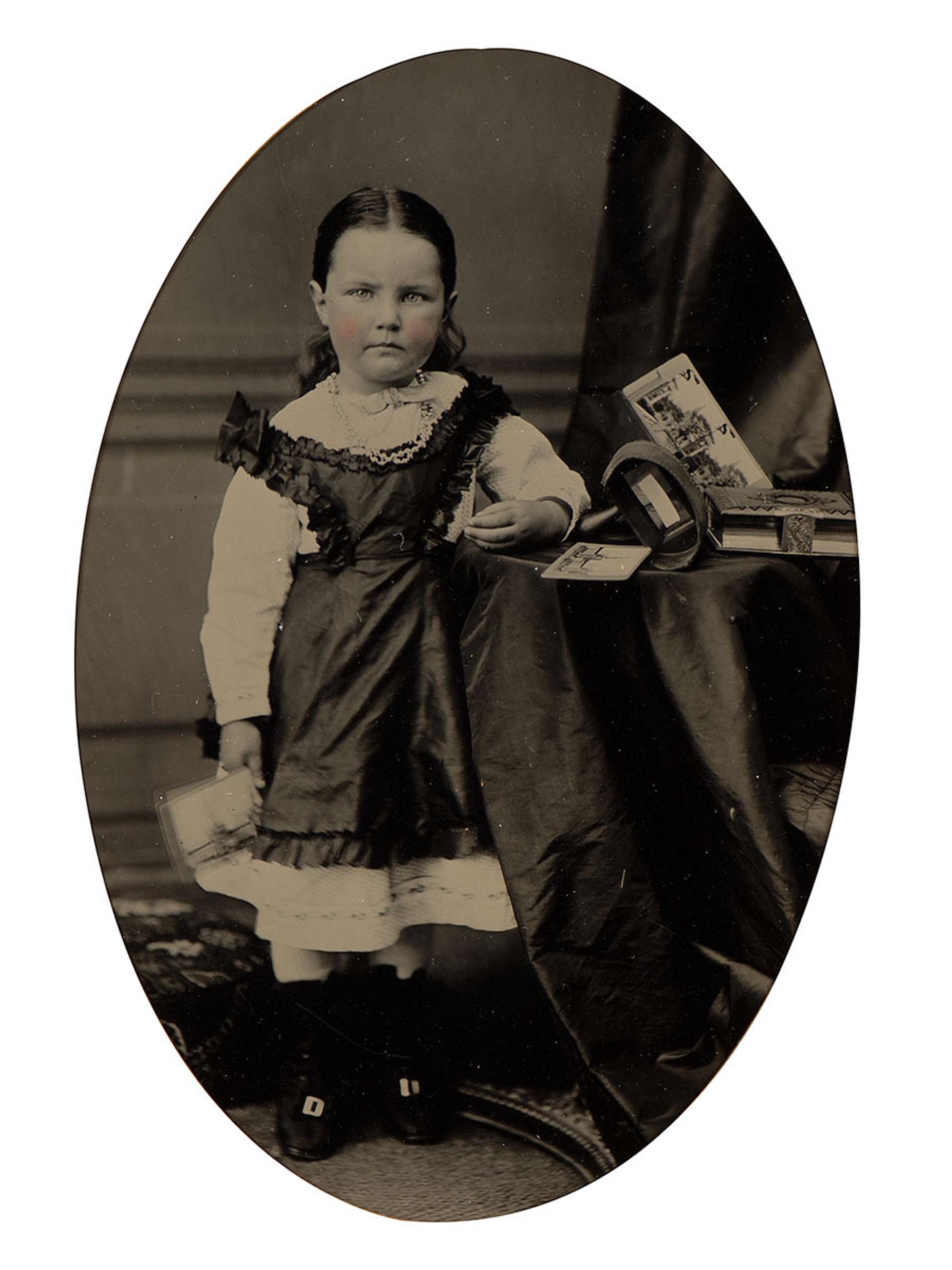 [EARLY PHOTOGRAPHY]. Tintype portrait of a little girl posed with stereoviews, viewer, and photo album.