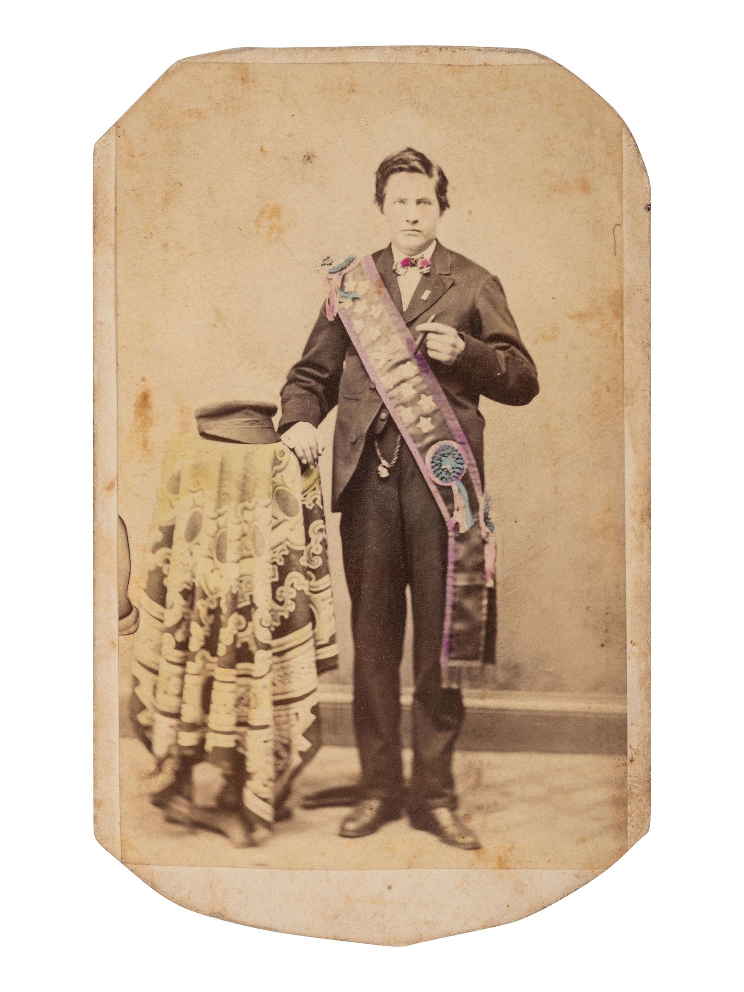[EARLY PHOTOGRAPHY]. CDV of a young man with a cigar and intricately-tinted sash with cockades.