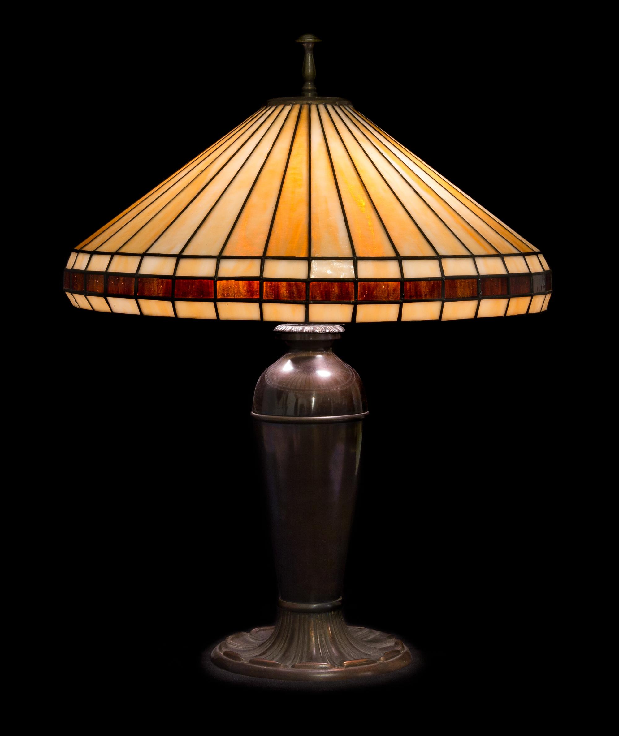 Miller Lamp Co., EARLY 20TH CENTURY, a leaded glass table lamp, having a conical geometric shade raised on an urn-form base